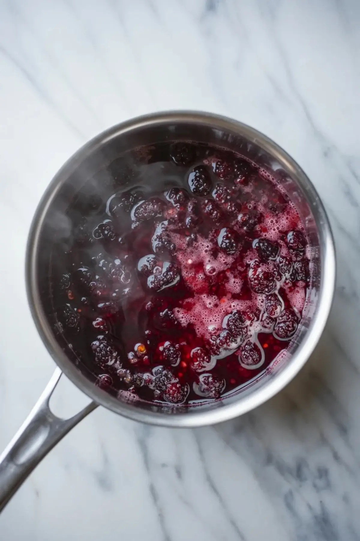 Mulberries simmering in a saucepan with sugar and lemon as the fruit cooks down for mulberry mousse cake filling.