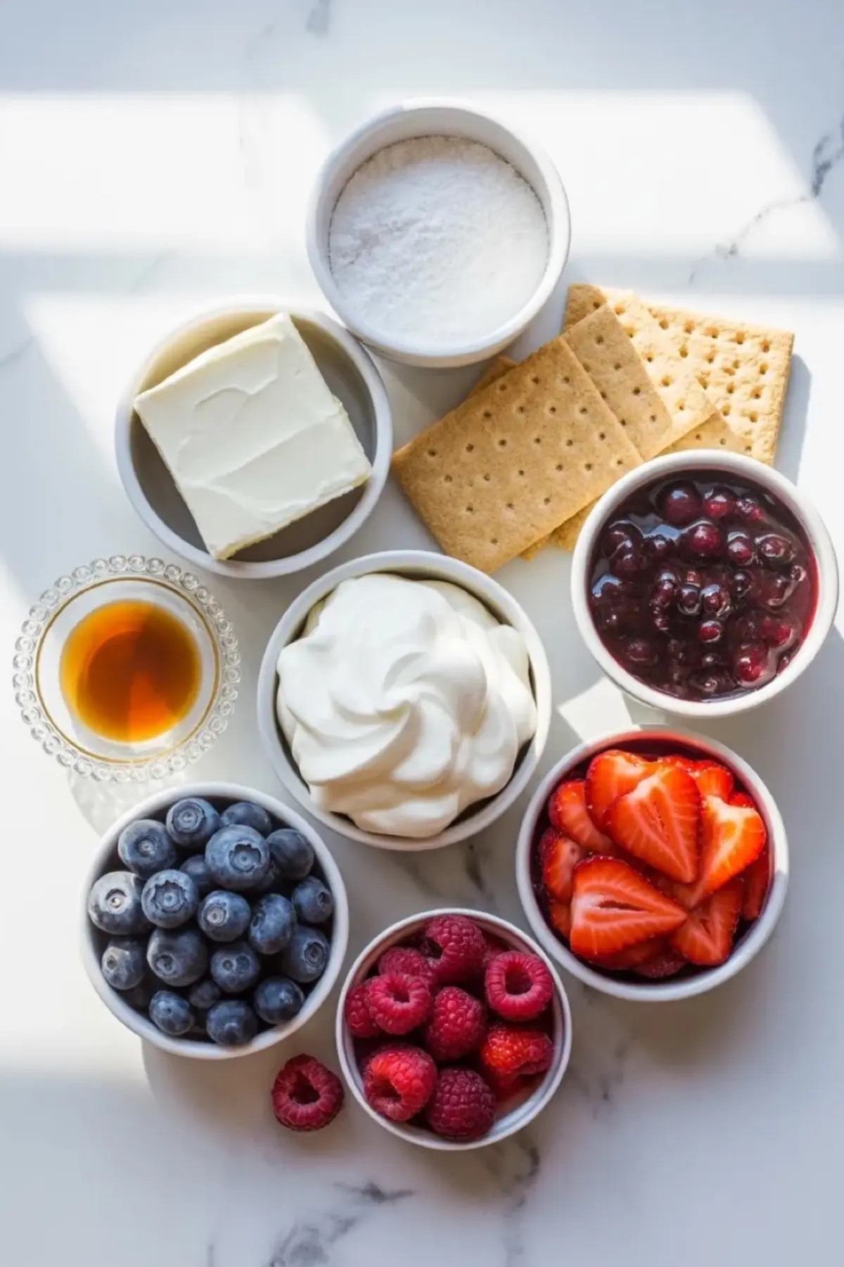 Ingredients for patriotic blueberry cheesecake icebox cake arranged with cream cheese, whipped topping, graham crackers, berries, sugar, vanilla, and blueberry filling.