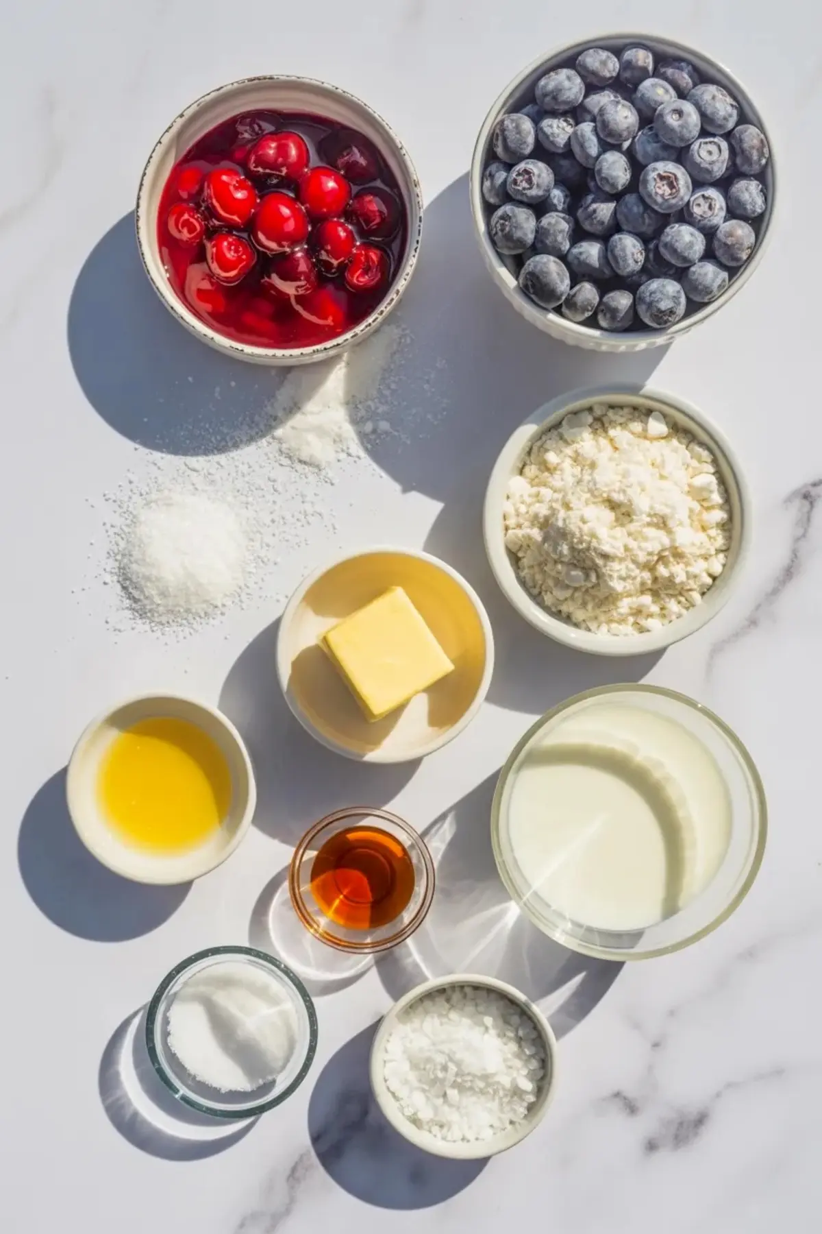 Ingredients for patriotic cherry cobbler arranged with cherries, blueberries, flour, sugar, butter, milk, cornstarch, and vanilla.