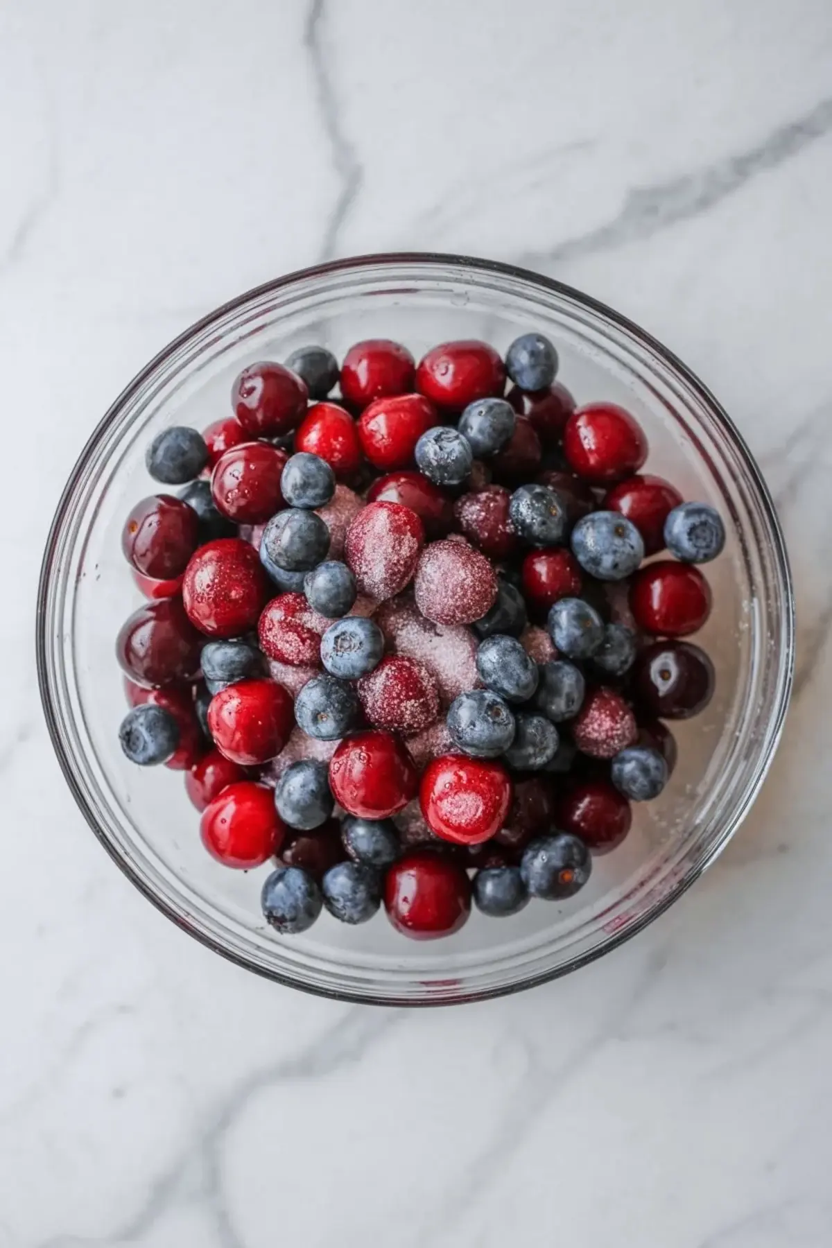 Cherries and blueberries tossed with sugar in a bowl for patriotic cherry cobbler filling before baking.