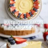 Patriotic lemon icebox pie topped with whipped cream, strawberries, and blueberries, shown whole and sliced on a plate.