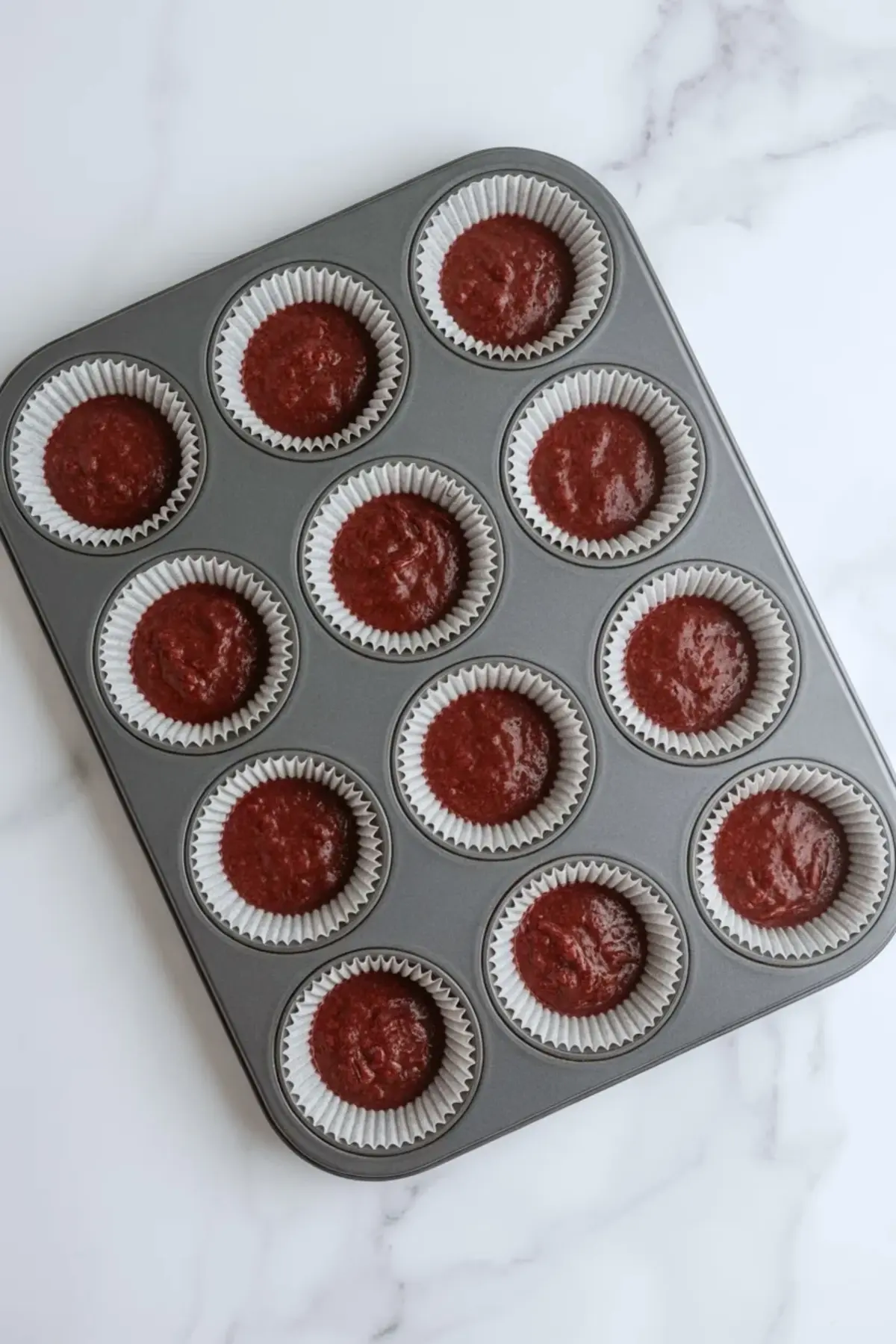 Red velvet cupcake batter portioned into lined muffin cups before baking.
