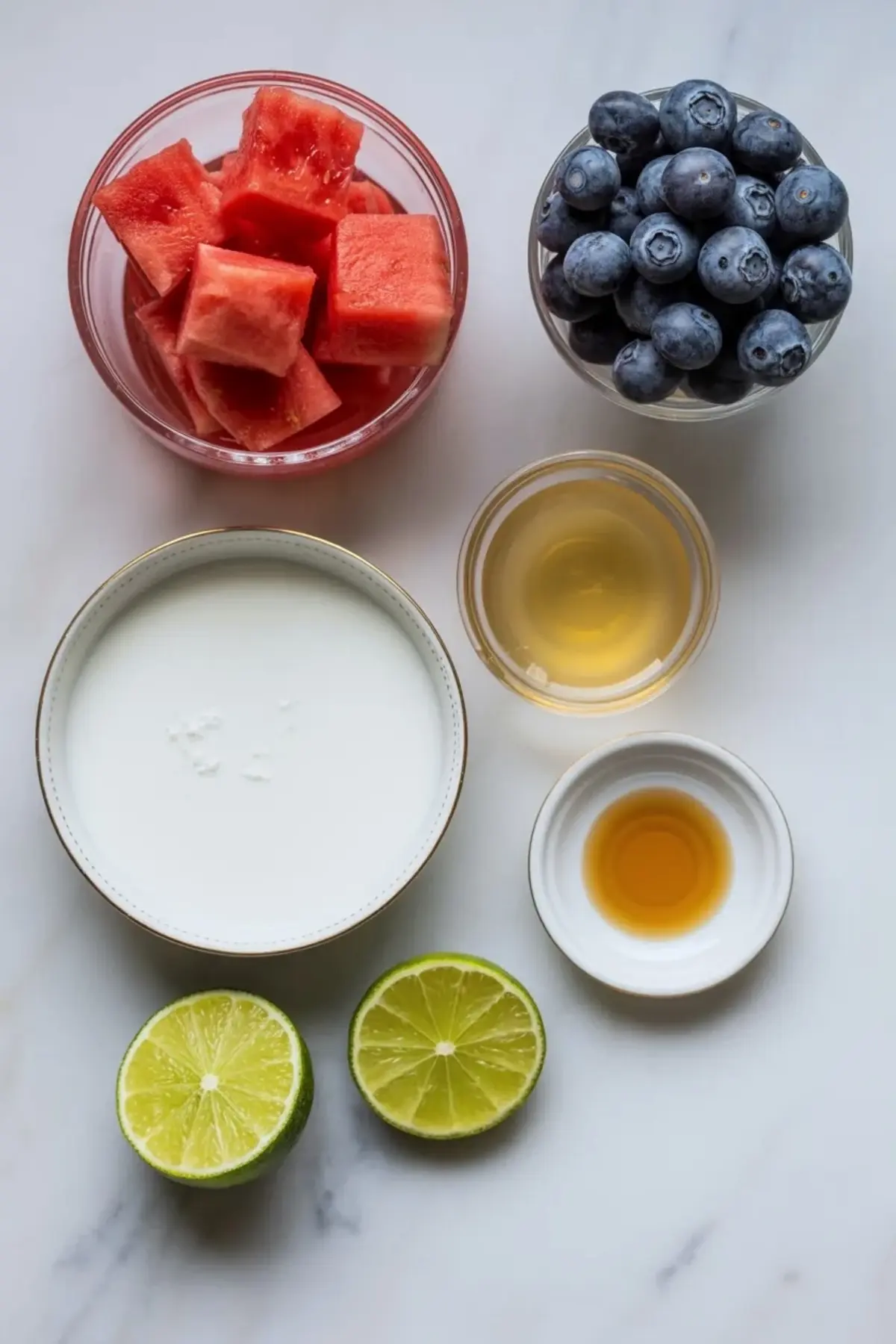 Ingredients for patriotic watermelon popsicles including watermelon, blueberries, coconut milk, lime, honey, and vanilla.