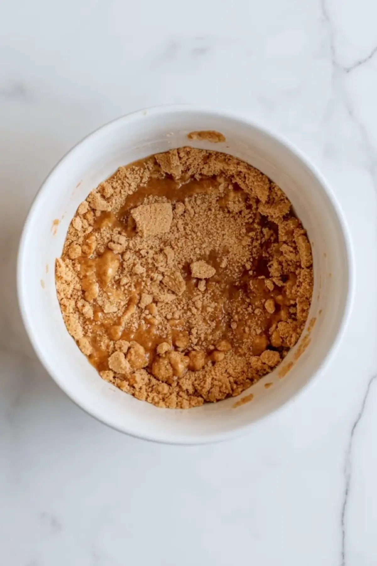 Cobbler crumble mixture in a white bowl for no-bake peach cobbler cheesecake bars, showing the buttery crumb topping before toasting.