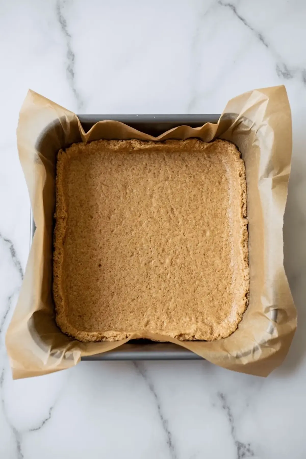 Ingredients for peanut butter smores bars arranged on white marble with graham cracker crumbs, peanut butter, chocolate, marshmallows, butter, sugar, and vanilla.