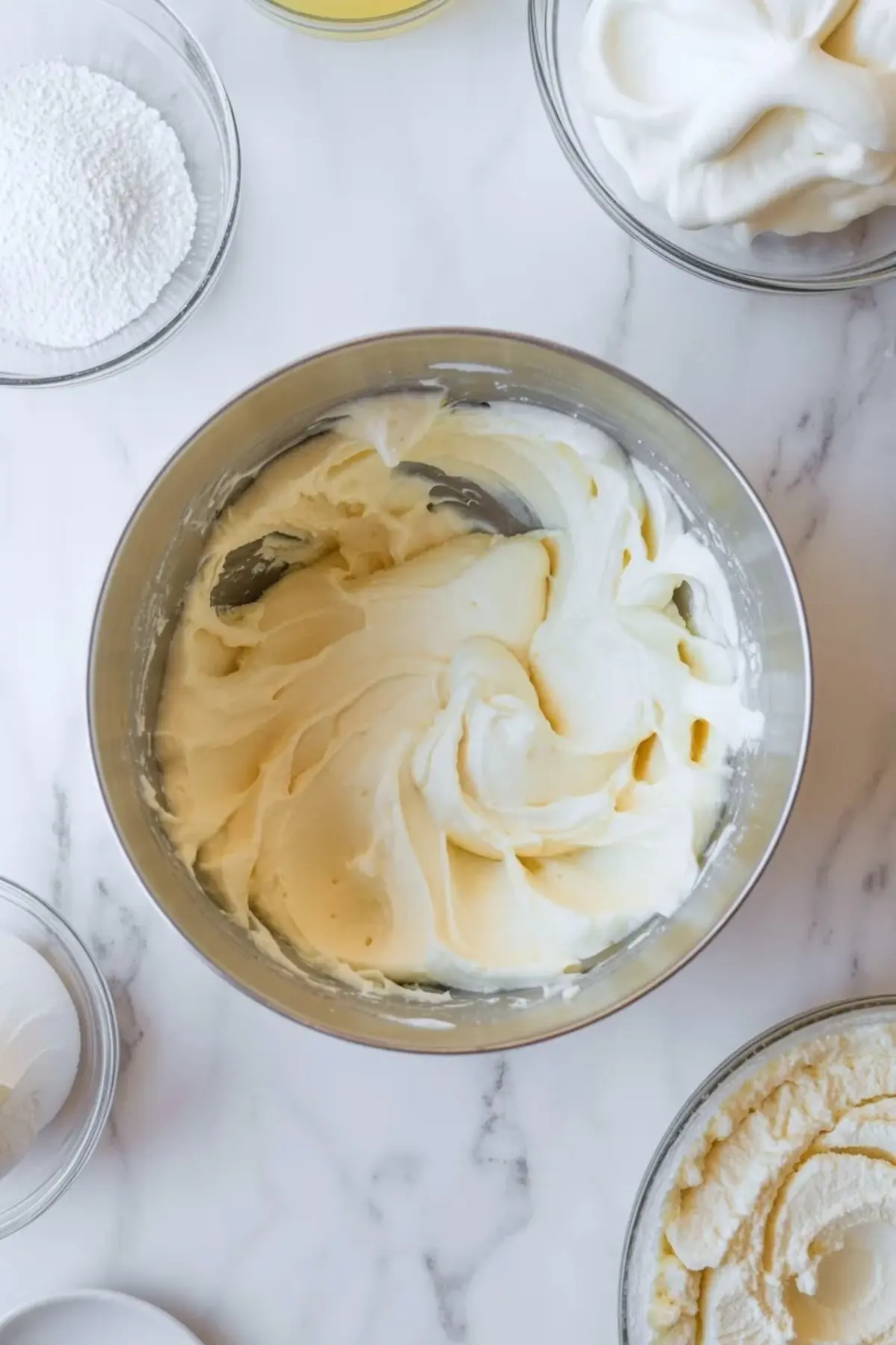 Cream cheese layer for pina colada lush whipped until smooth in a bowl with powdered sugar and whipped topping nearby on white marble.