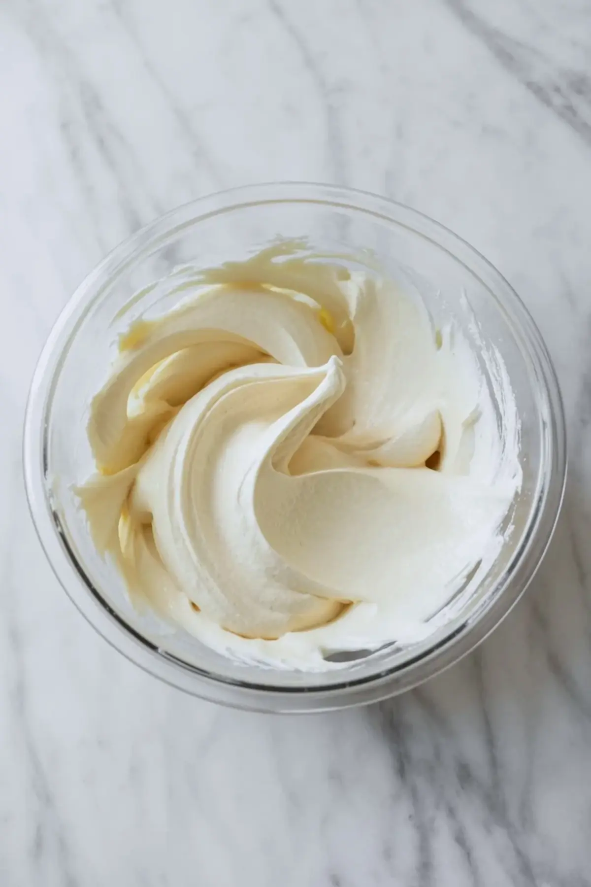 Cream cheese filling for pineapple lush dessert whipped until smooth in a glass bowl on a white marble surface.