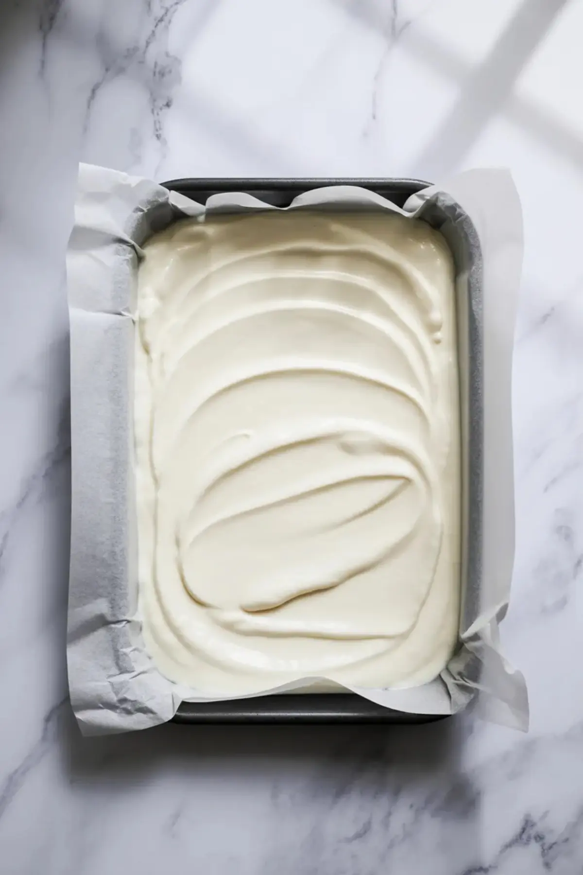 Greek yogurt base for strawberry yogurt bark is spread in a parchment lined pan before the strawberry swirl and almond topping are added.