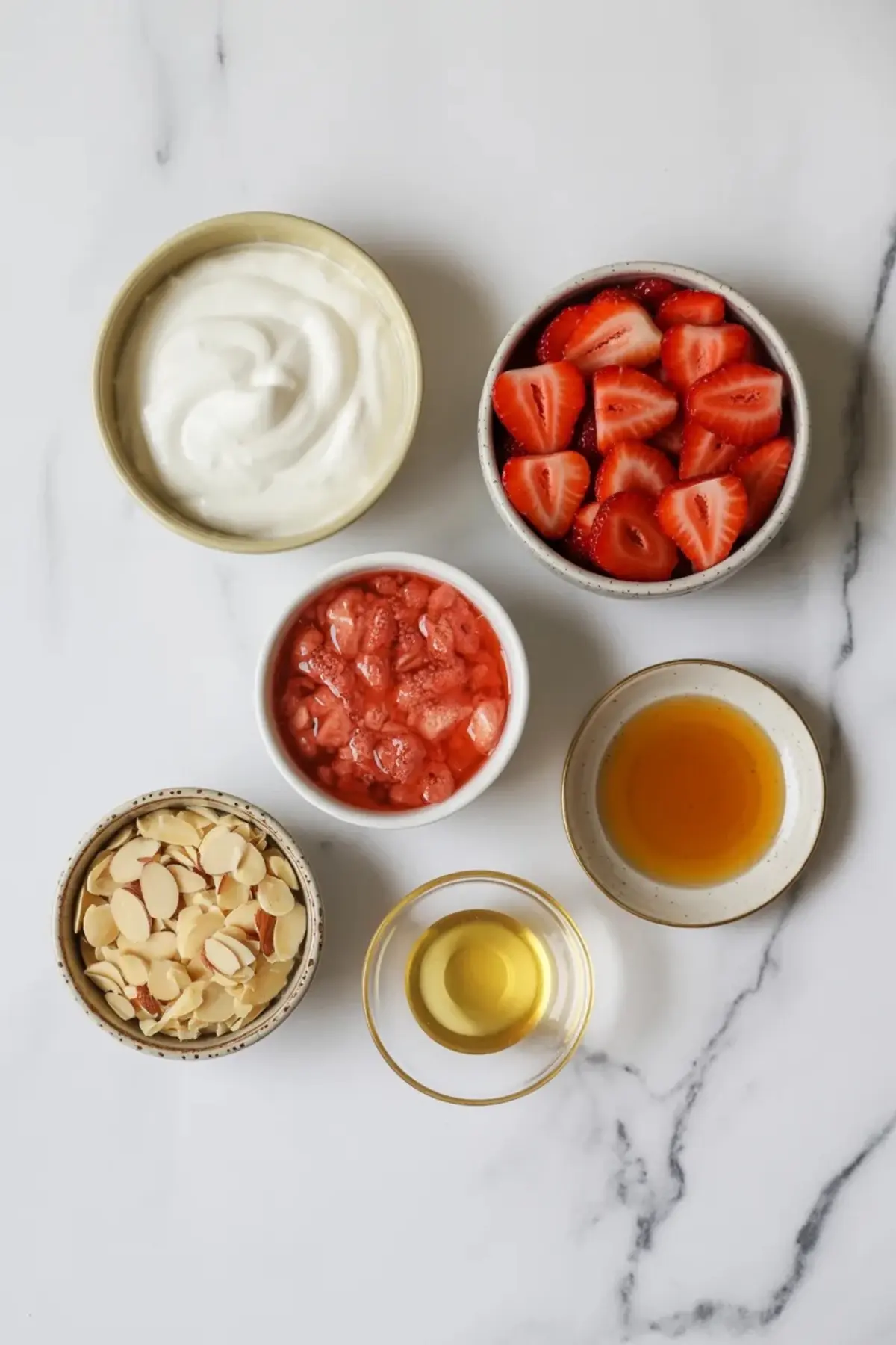 Ingredients for strawberry yogurt bark are arranged in bowls with Greek yogurt, fresh strawberries, mashed strawberries, honey, vanilla, and sliced almonds.
