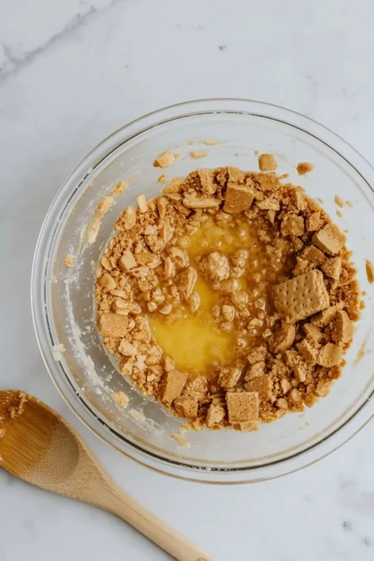 Graham cracker crust mixture in a glass bowl for small-batch strawberry mousse cheesecake bars, showing crumbs, sugar, and melted butter before pressing into the pan.