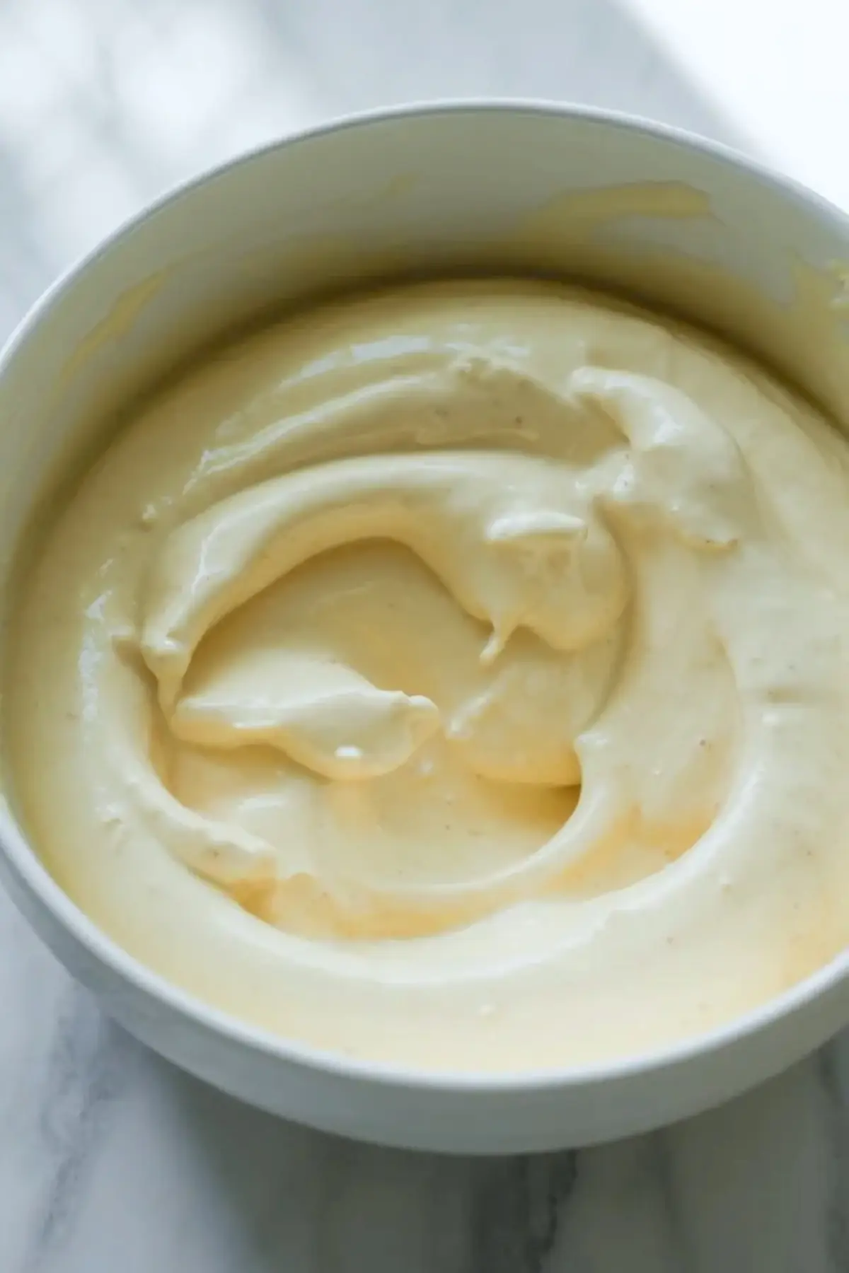 Mascarpone cream filling for strawberry tiramisu in a white bowl on a marble surface before layering.