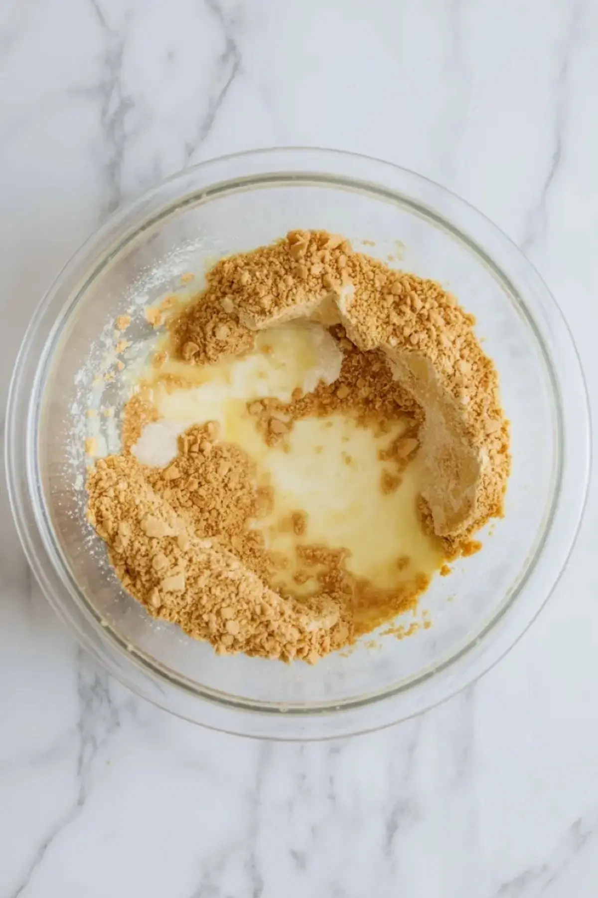 Pressed vanilla wafer crust in a parchment lined square pan for banana pudding bars on a white marble surface.