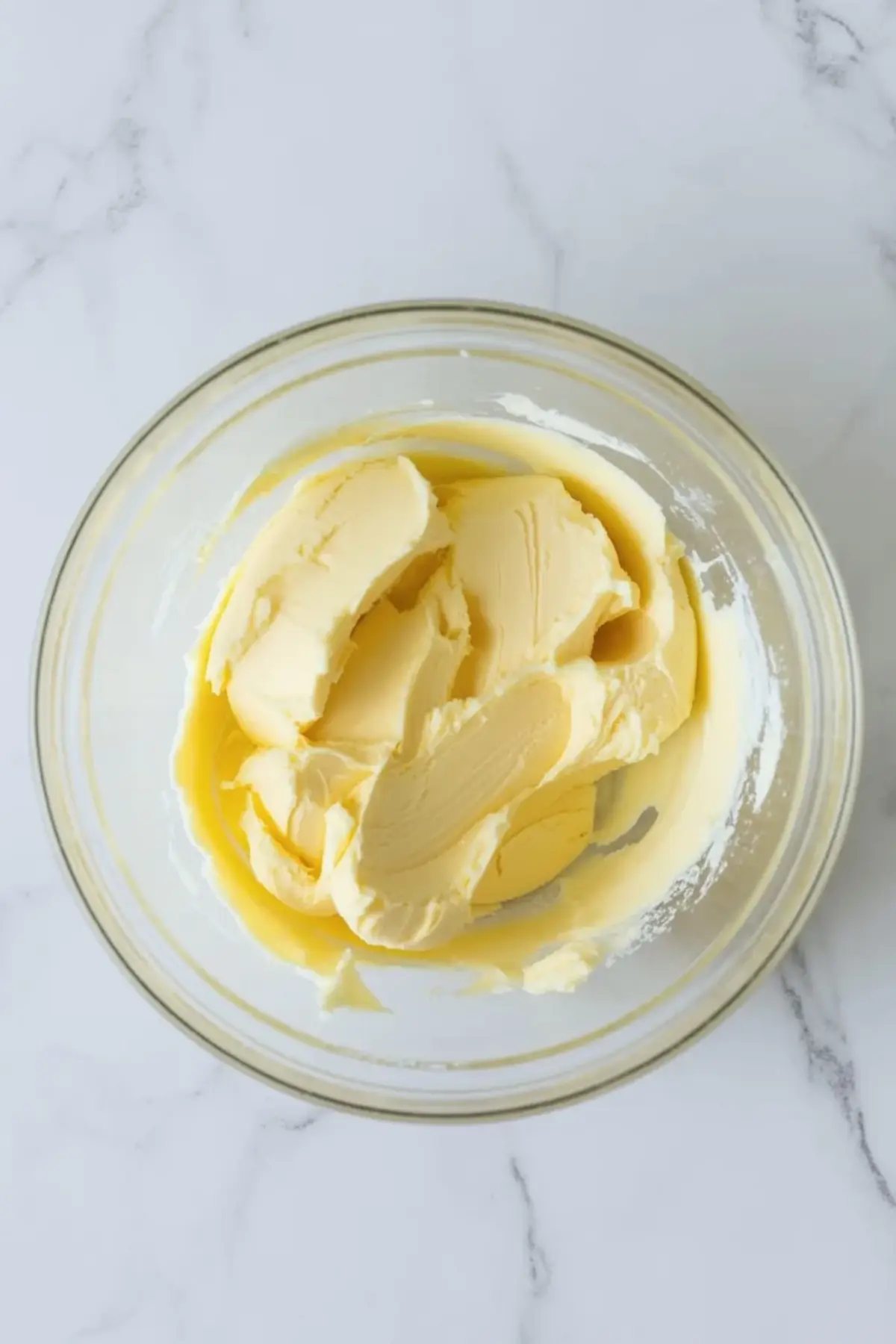 Softened butter in a glass bowl ready for almond buttercream frosting at the start of mixing.