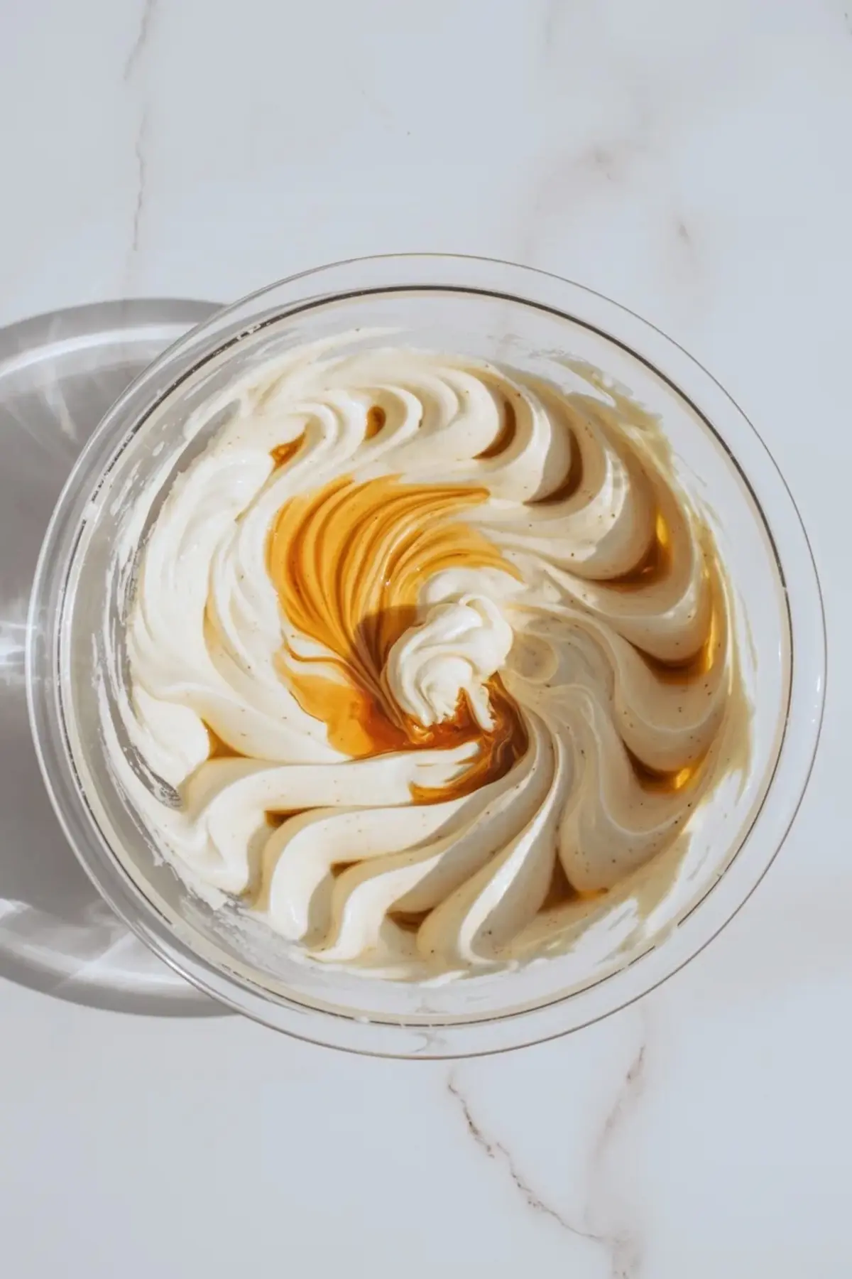 Almond buttercream frosting partially whipped in a bowl as flavoring is mixed in for a smooth fluffy texture.