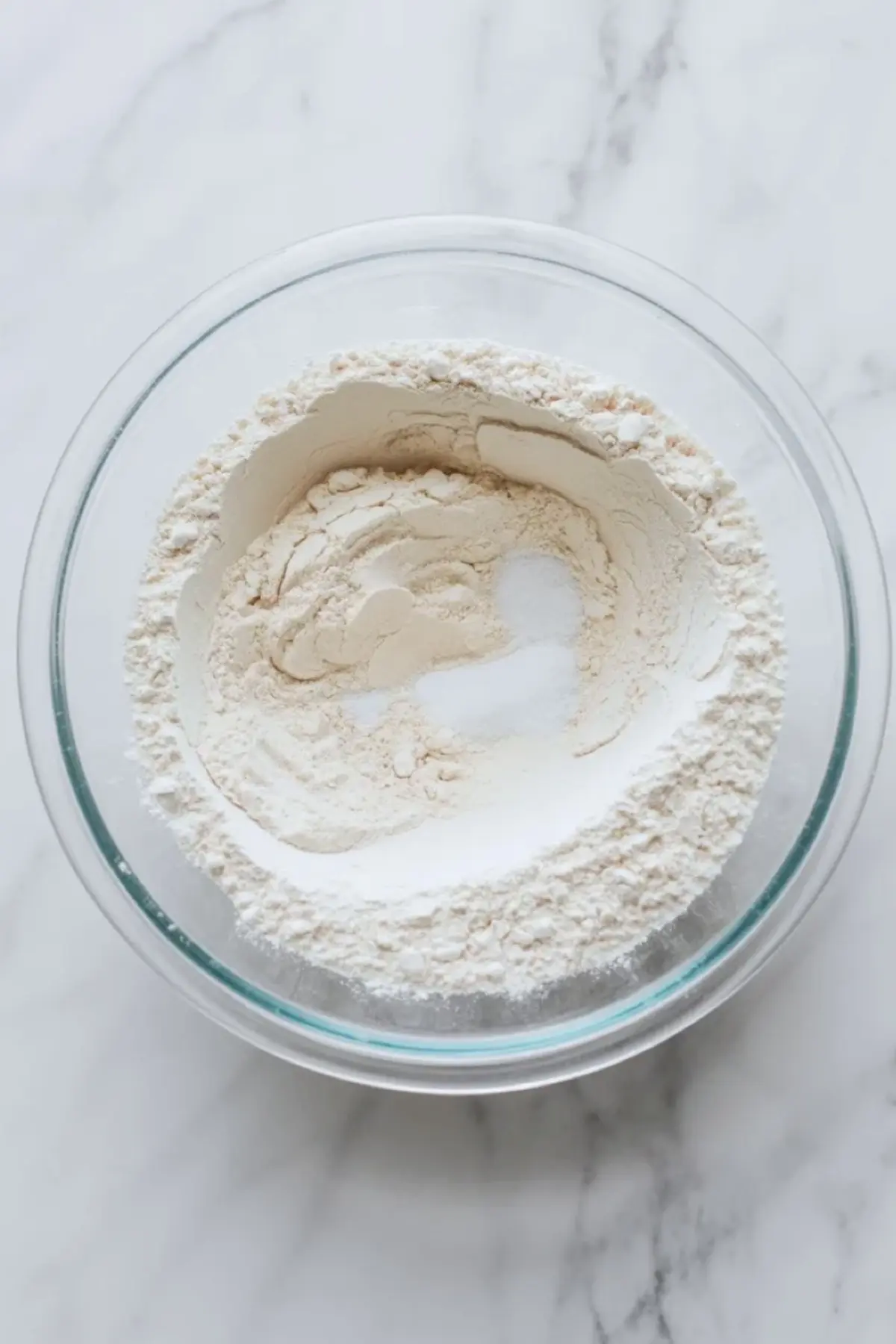 Flour, baking powder, and salt sit in a glass bowl as the dry ingredients for American flag cake are prepared.