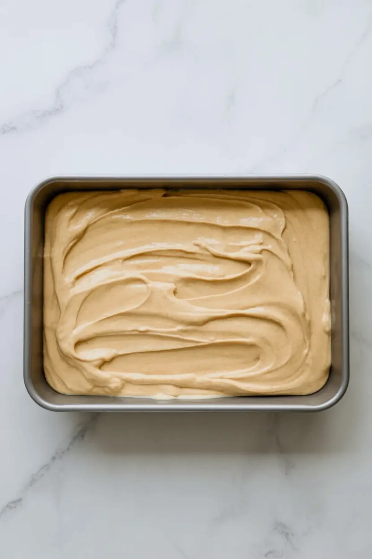 American flag cake batter is spread evenly in a rectangular pan before baking into a holiday sheet cake.