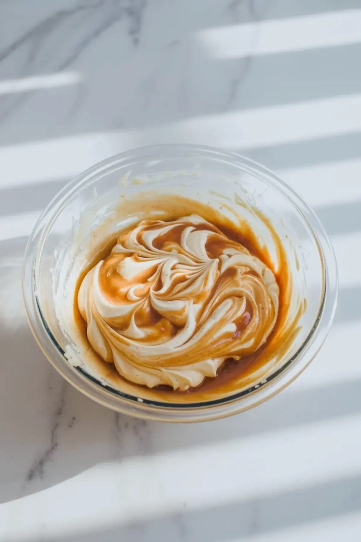 Partially mixed apple butter frosting in a glass bowl showing the smooth spiced texture as it finishes blending.
