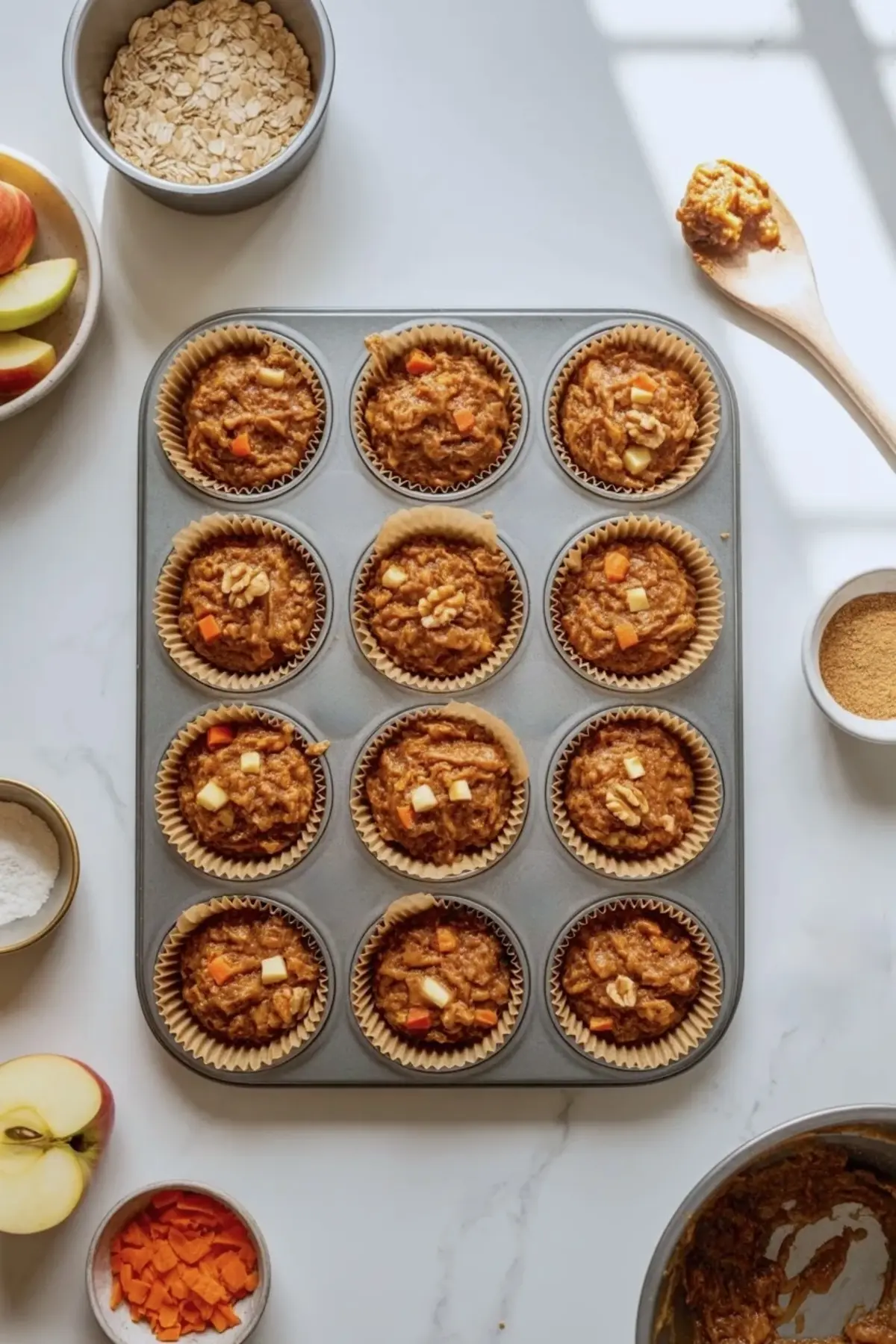 Apple carrot muffin batter portioned into a lined muffin tin with visible apple pieces and carrot shreds before baking.