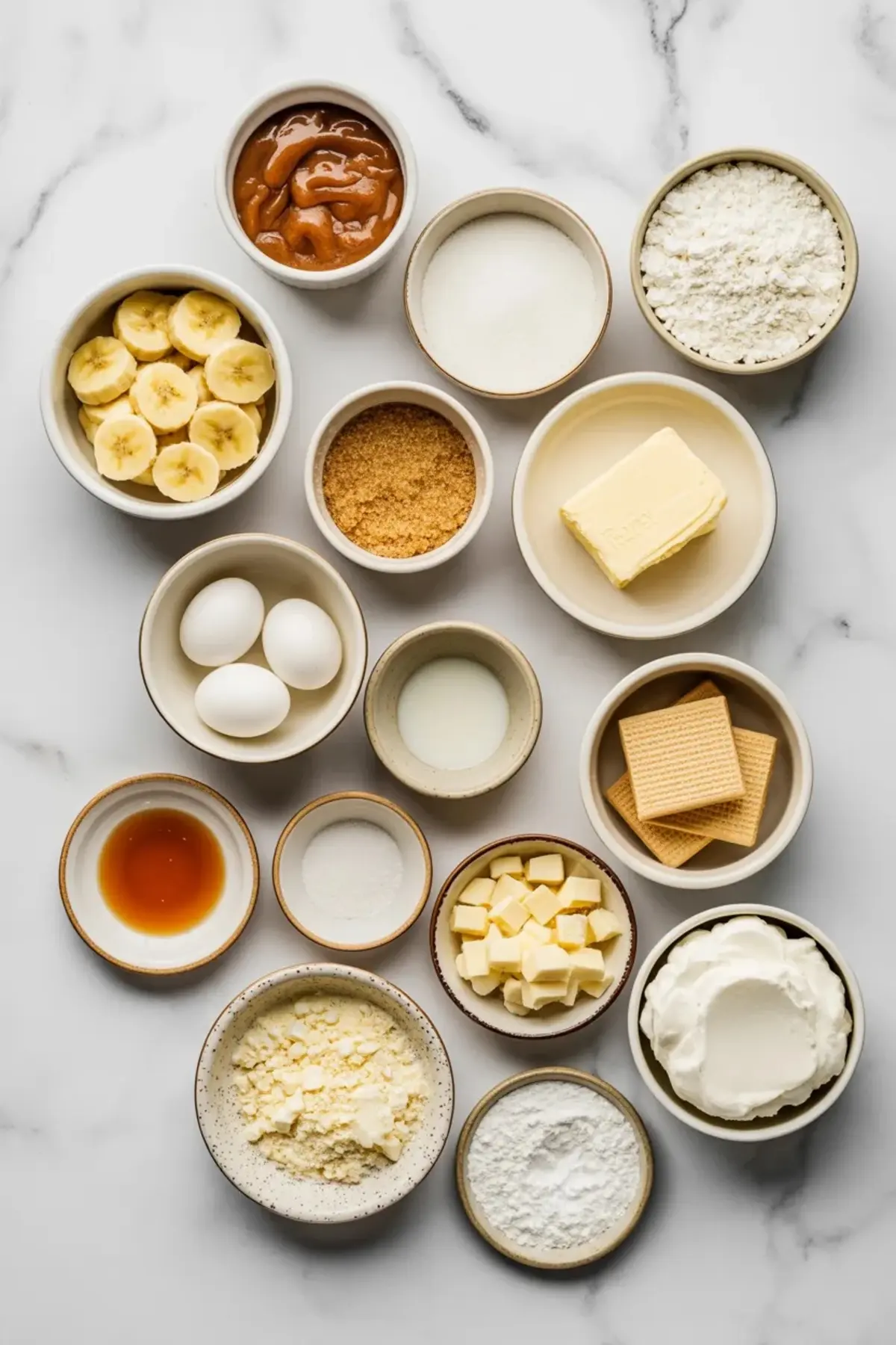 Ingredients for banana pudding cookies arranged overhead with bananas, eggs, butter, flour, pudding mix, vanilla wafers, white chocolate chips, and cream cheese filling ingredients.