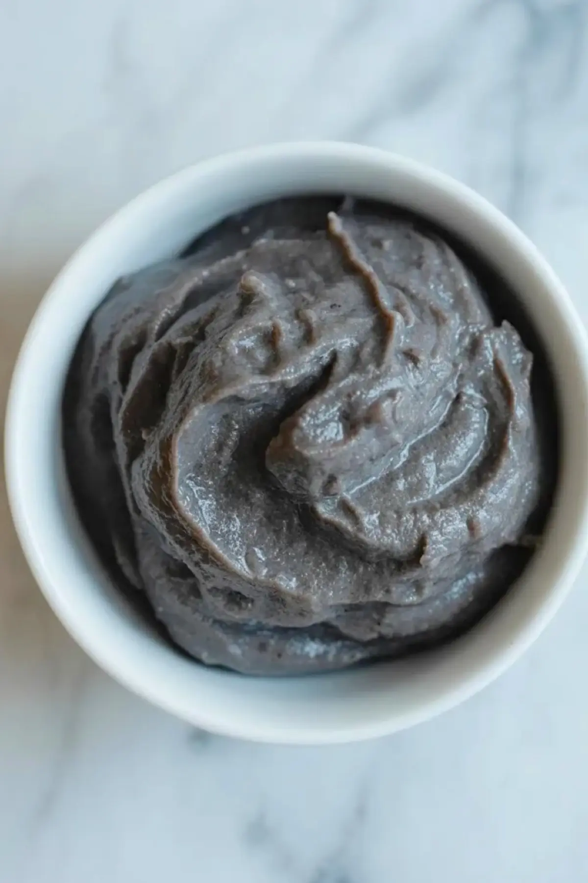 Black sesame paste sits in a white ramekin after the toasted seeds have been ground for homemade black sesame ice cream.