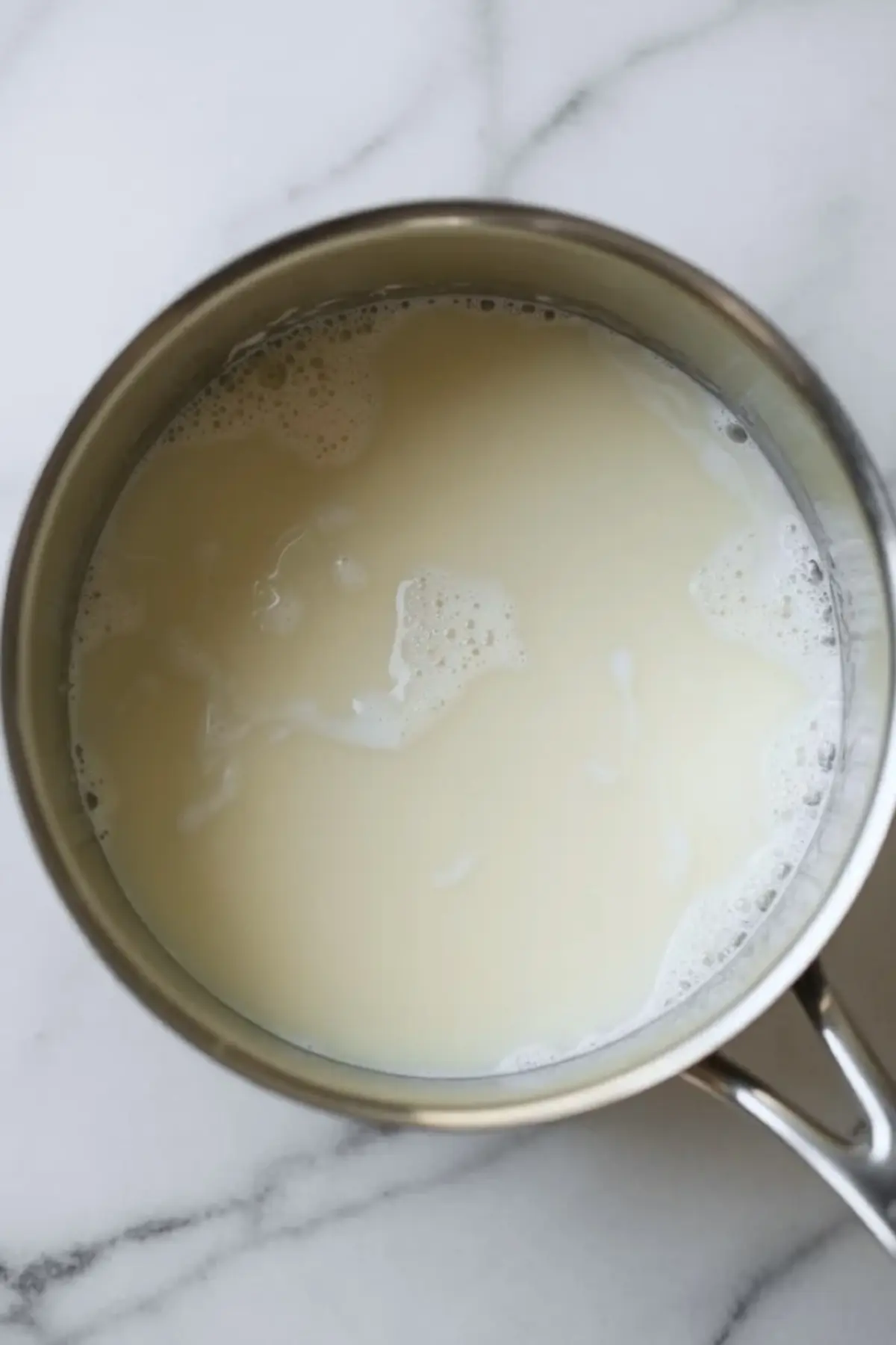Milk and cream warm in a saucepan while the custard base for black sesame ice cream is prepared.