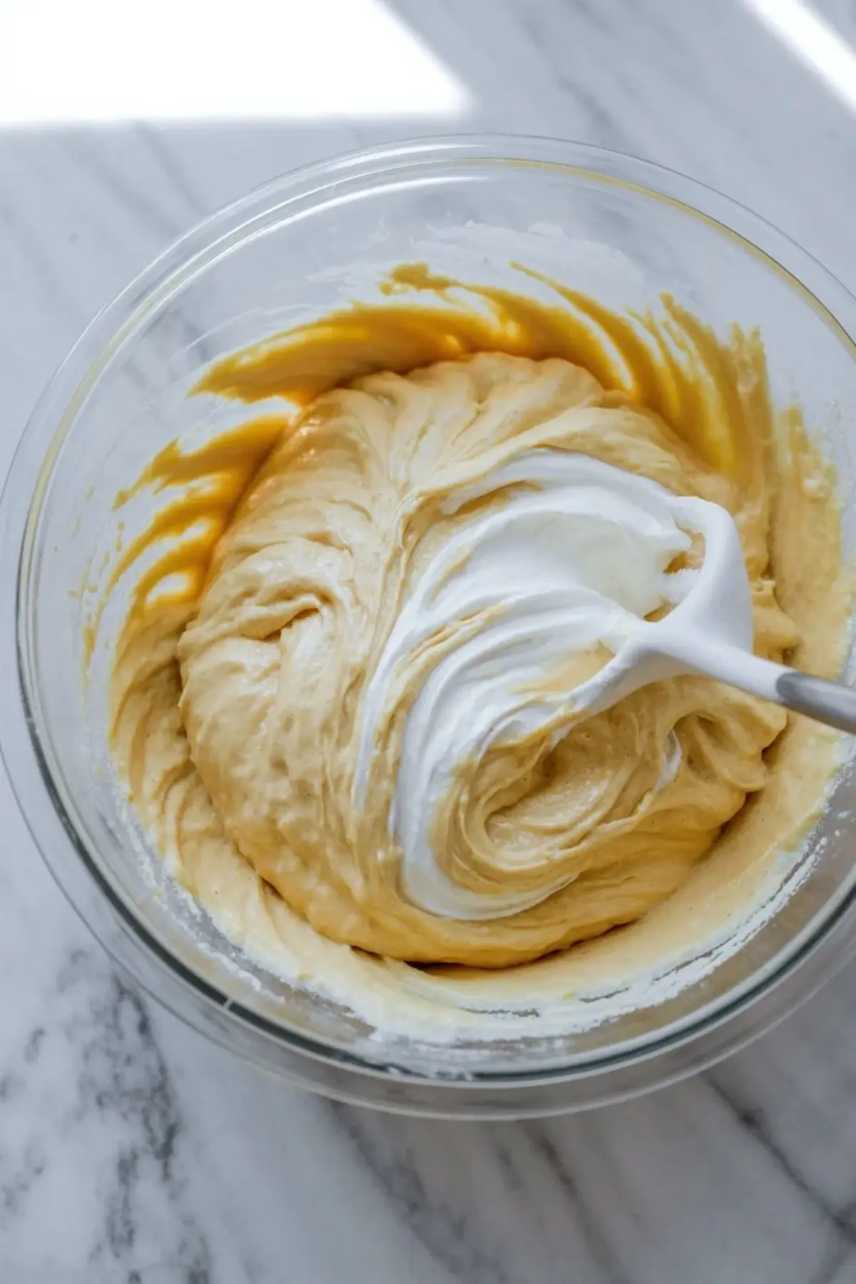 Sour cream is folded into blueberry coffee cake batter in a mixing bowl to keep the crumb soft and moist.