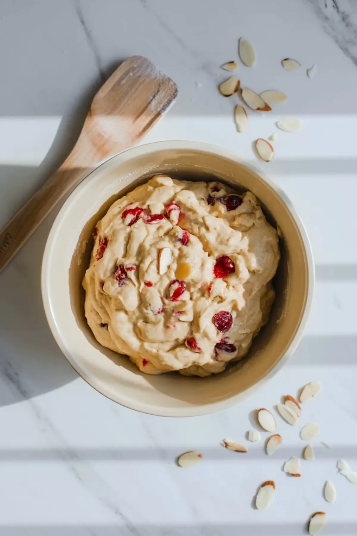 Cherry almond cookie dough in a bowl with visible cherry pieces and sliced almonds before chilling and baking.