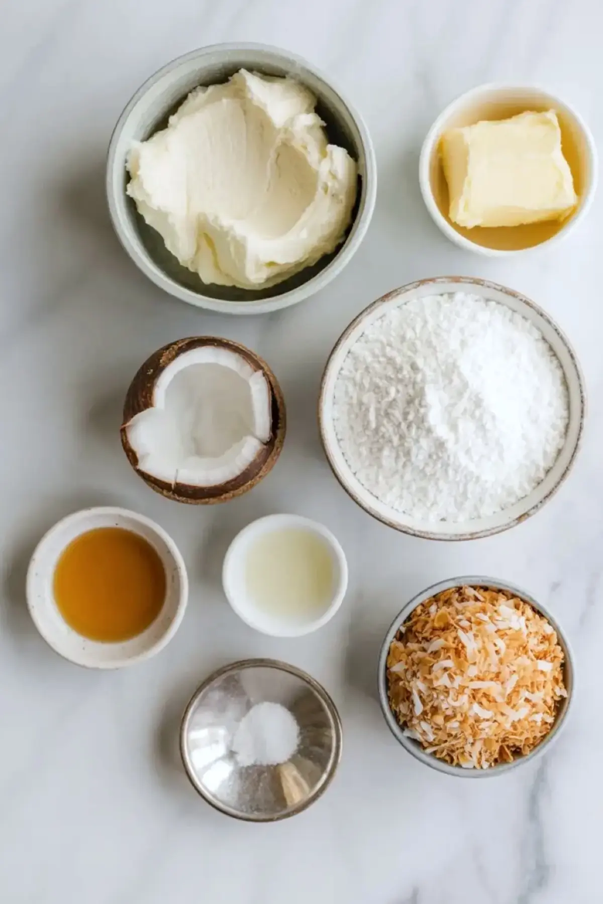 Ingredients for coconut cream cheese frosting arranged overhead with cream cheese, butter, powdered sugar, coconut cream, vanilla, salt, and toasted coconut flakes.