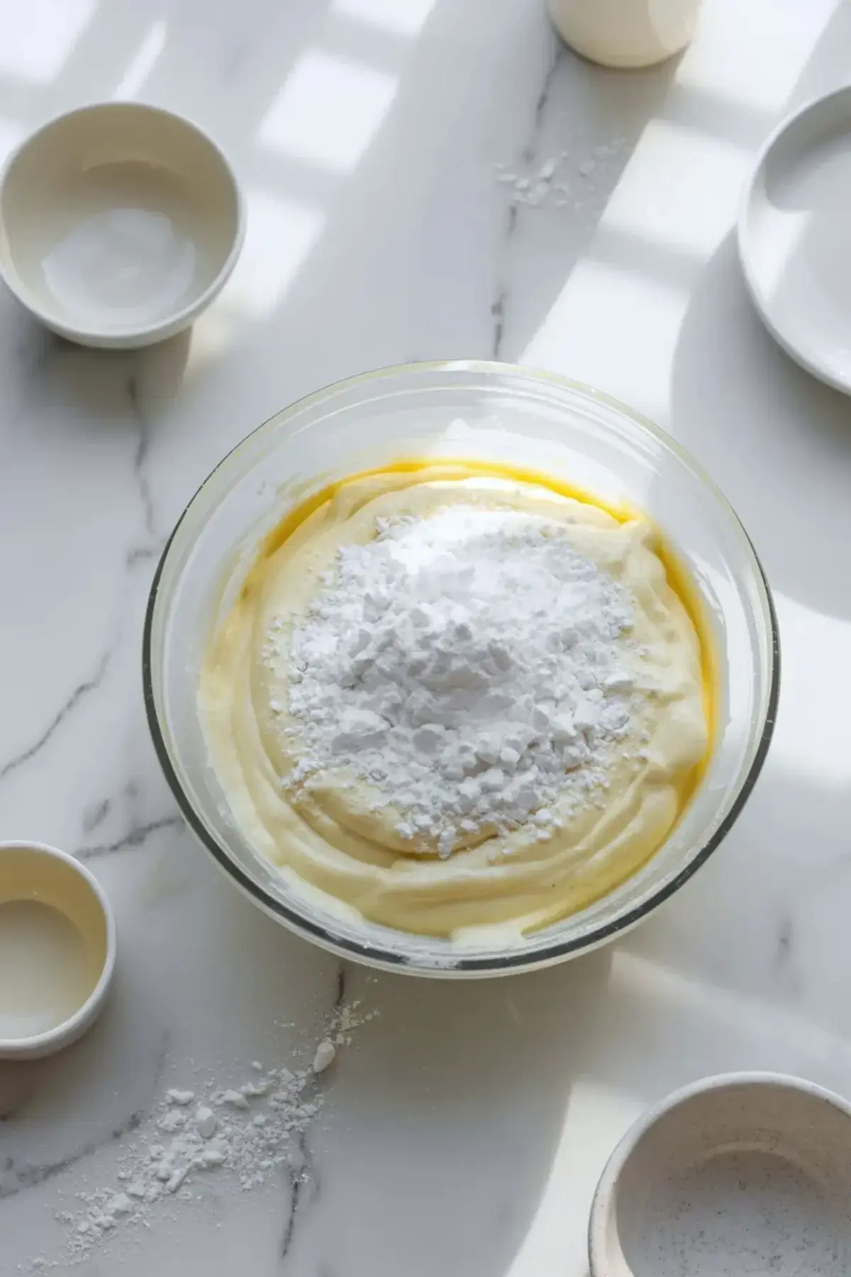 Powdered sugar added to a bowl of coconut cream cheese frosting as the mixture is being whipped to a smooth pipeable texture.