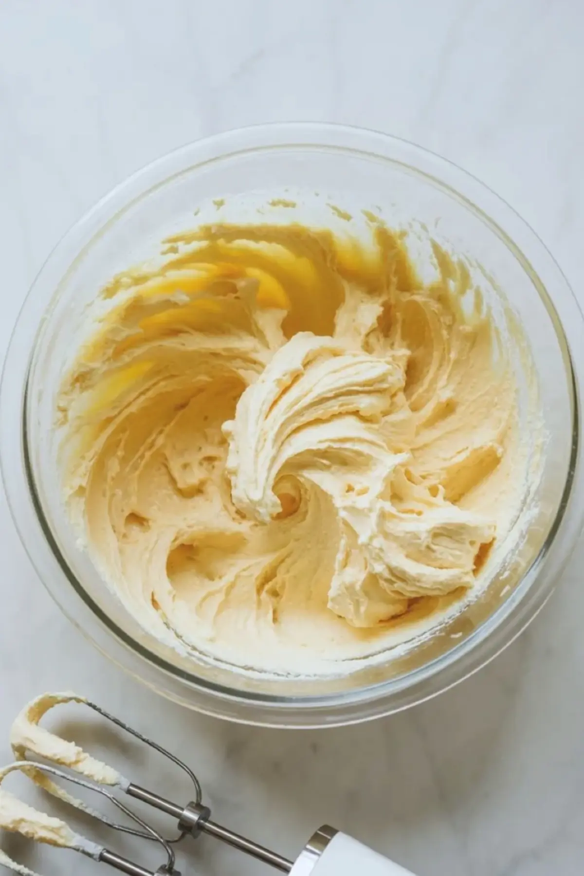 Whipped butter and cream cheese mixture for coconut cream cheese pound cake in a glass bowl with mixer beaters on a light marble surface.