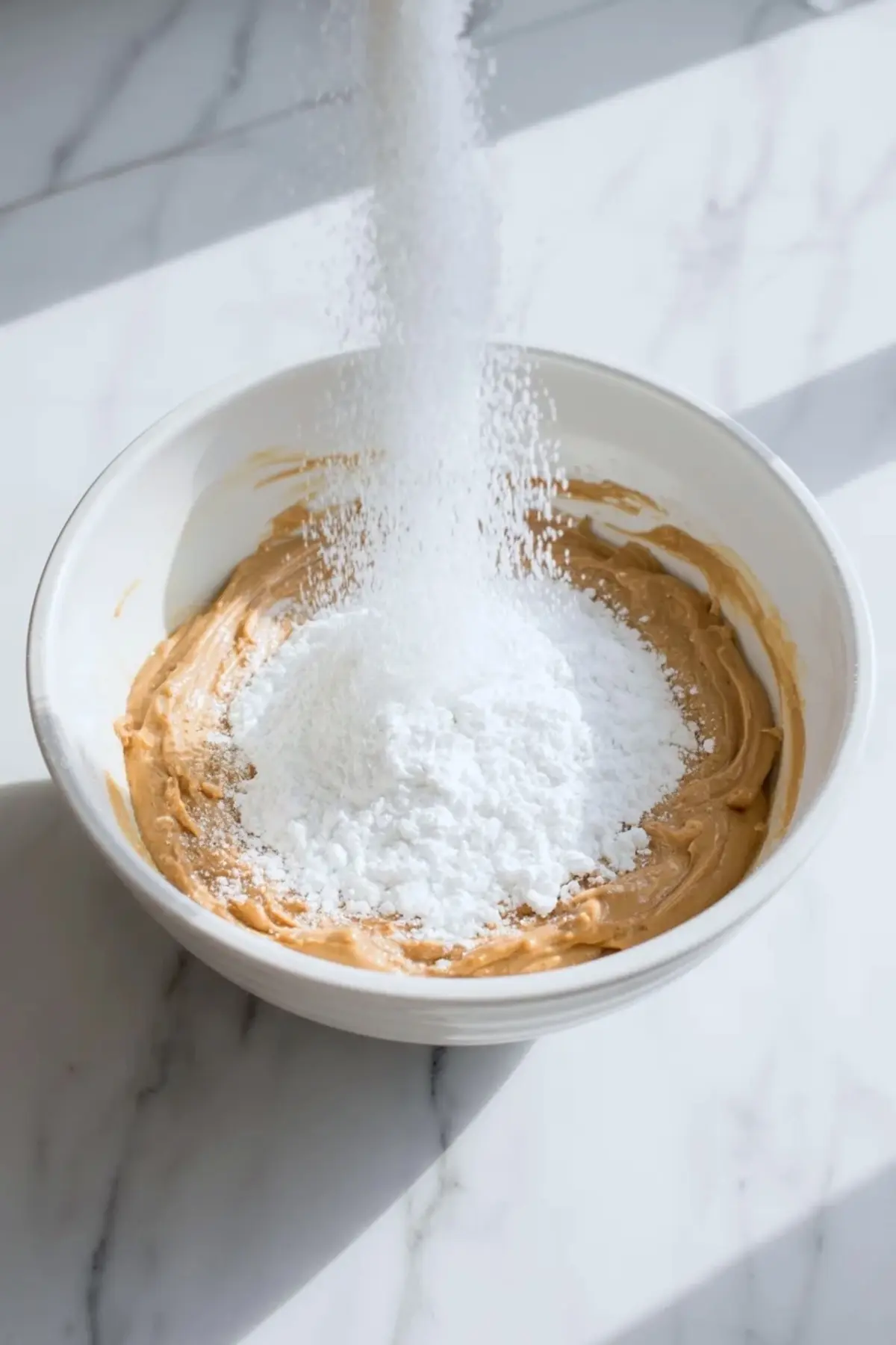 Powdered sugar is being added to cookie butter frosting in a mixing bowl as the buttercream comes together.