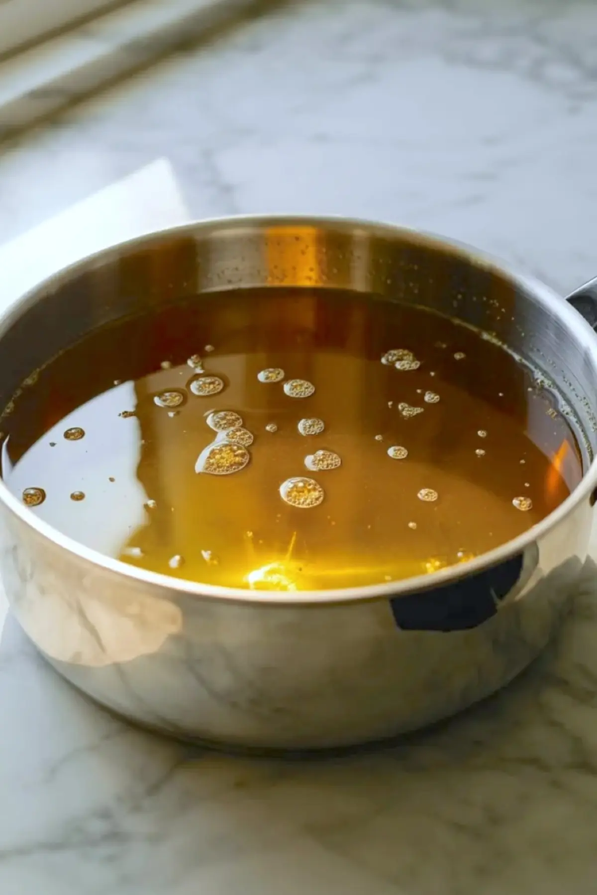 Golden dandelion honey syrup simmering in a saucepan after straining and reducing.