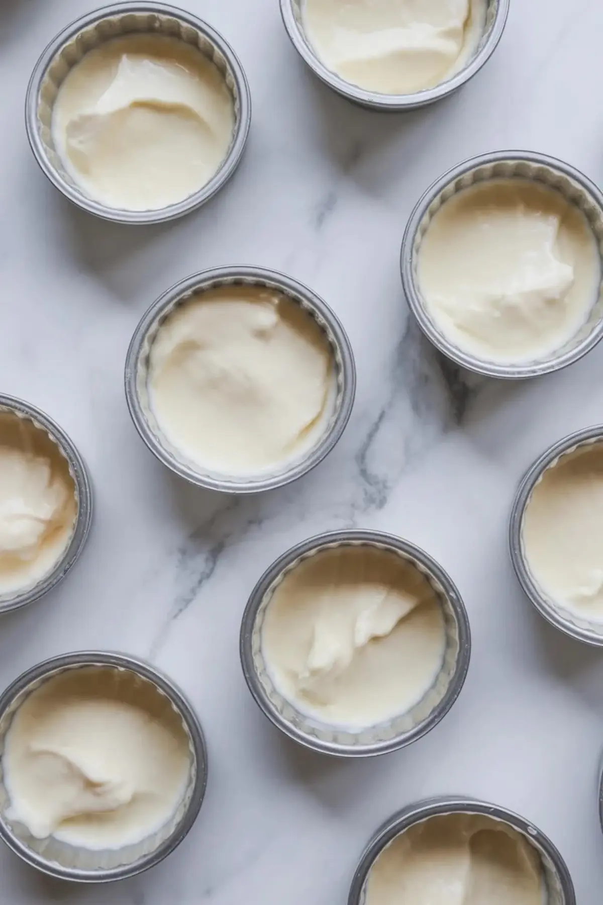 Frozen yogurt raspberry bites portioned into small round molds with creamy filling ready to freeze on a marble surface.