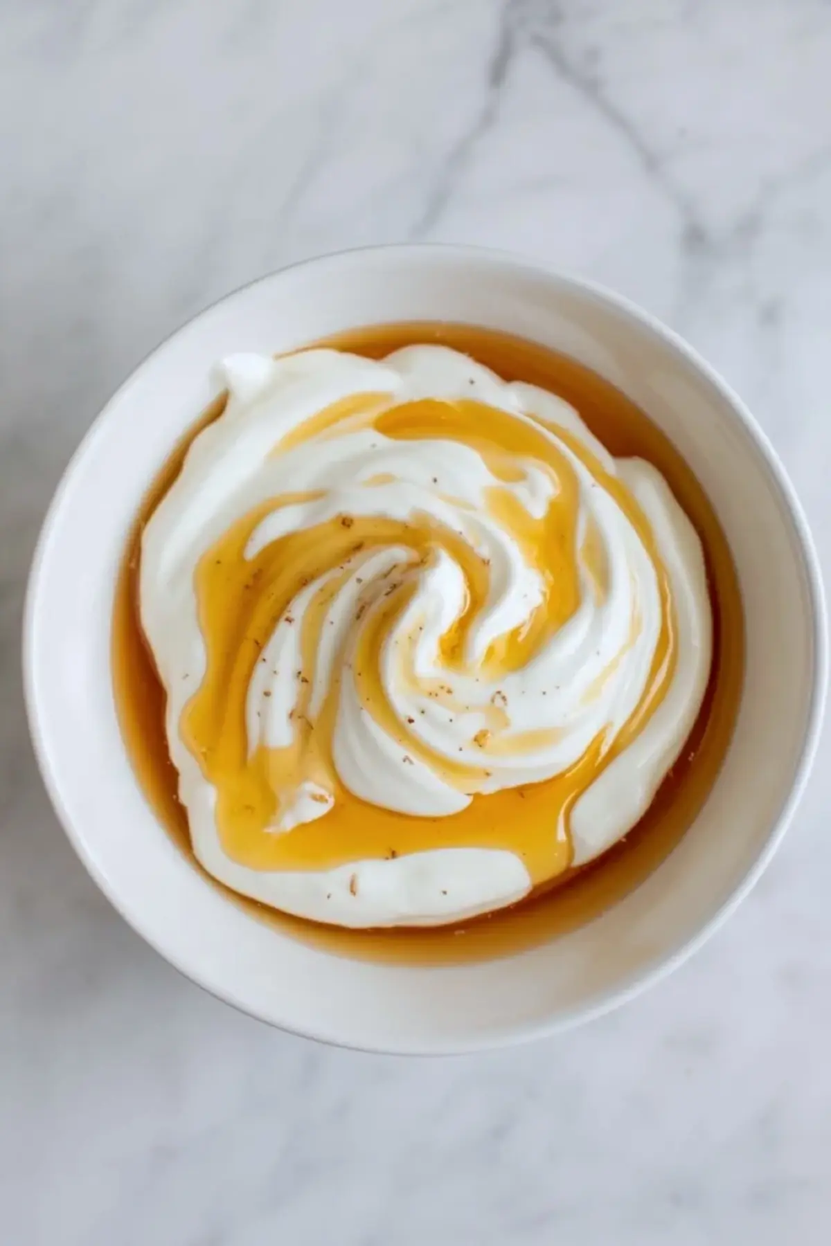Greek yogurt mixed with honey for frozen yogurt raspberry bites in a white bowl on a light marble surface.
