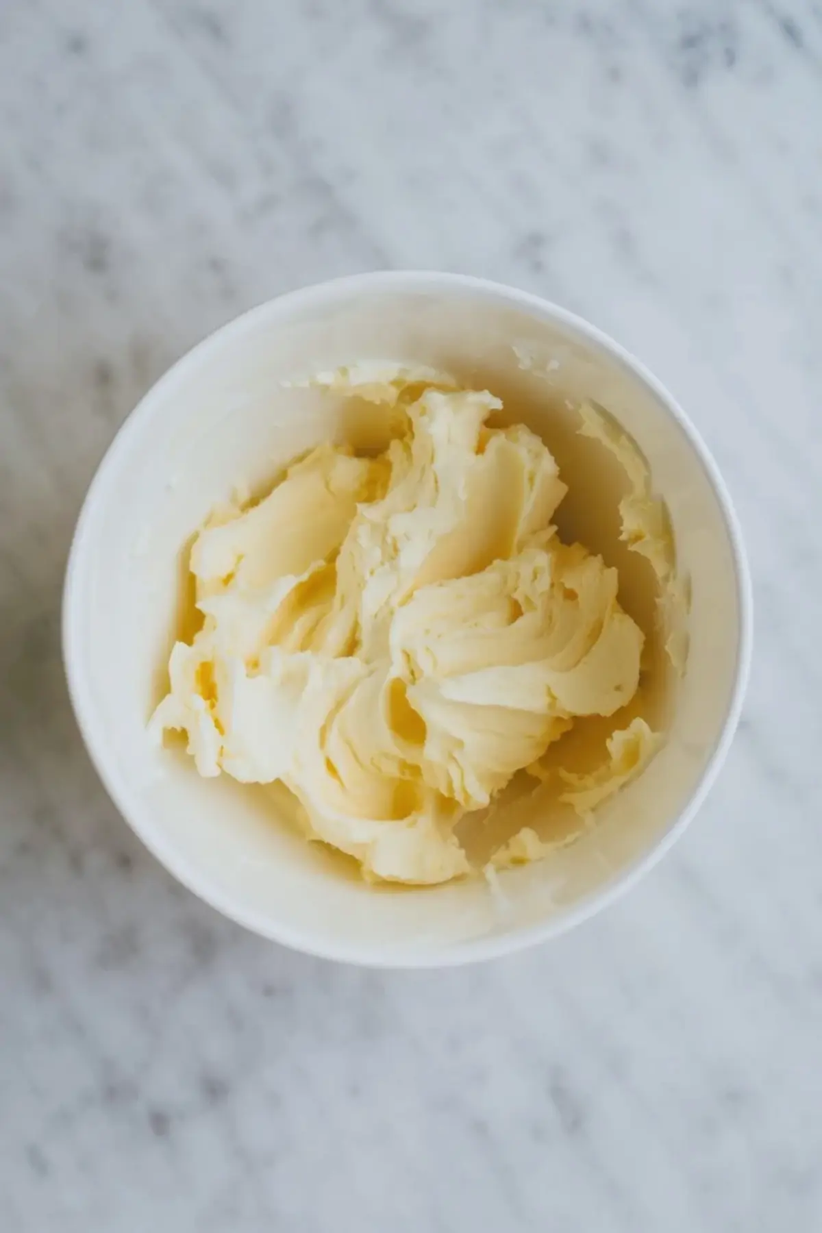Softened butter beaten in a glass mixing bowl on white marble to start hazelnut praline cream frosting.