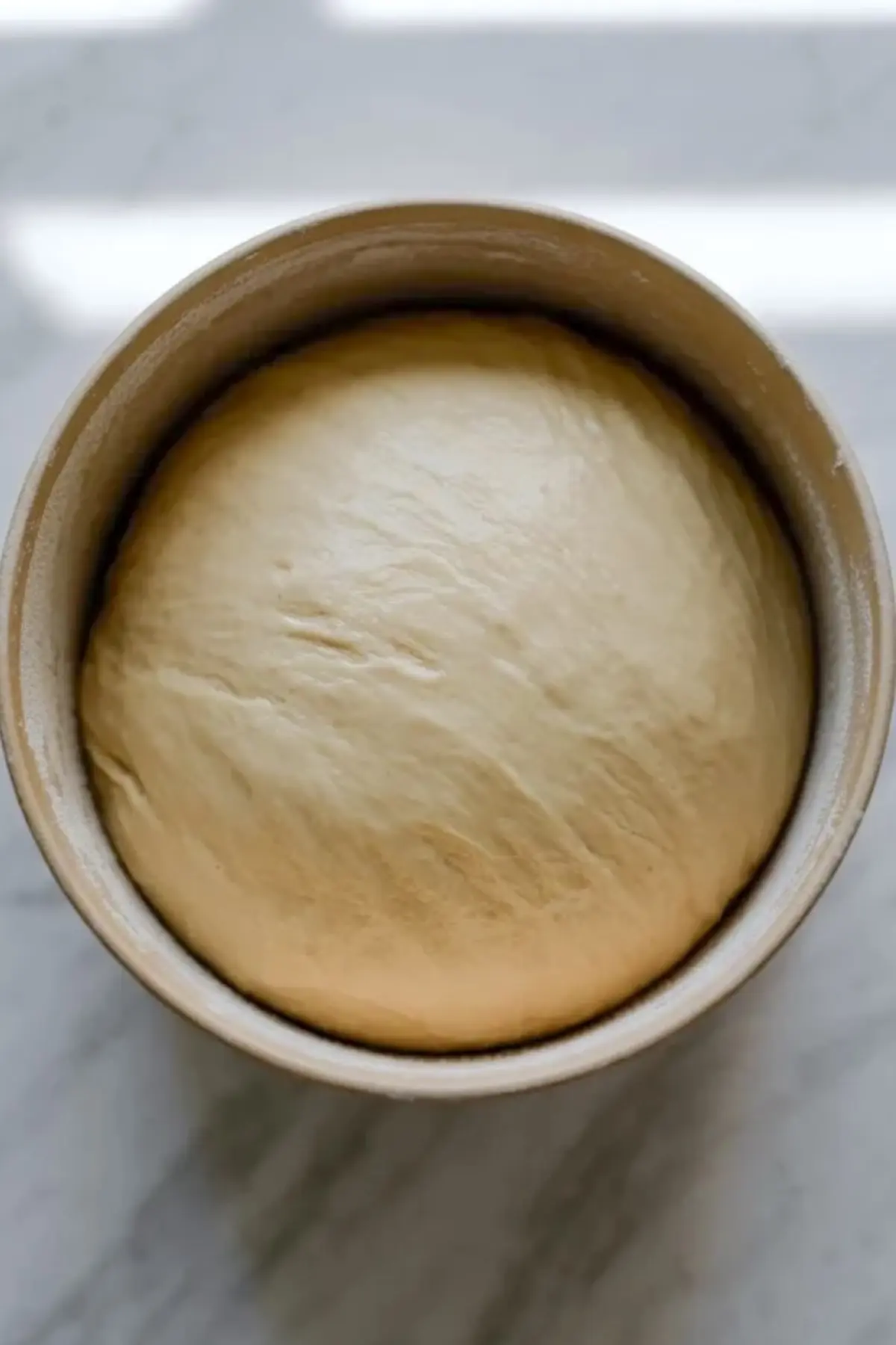 Proofed Hokkaido milk bread dough rests in a bowl after the first rise and looks smooth and airy.