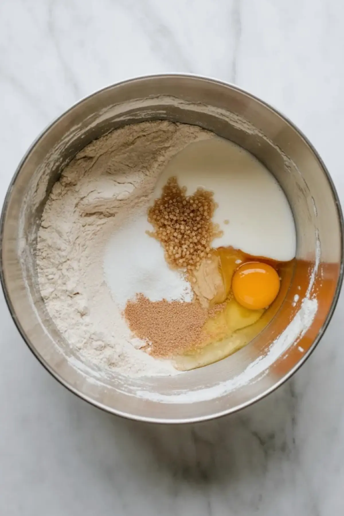 Hokkaido milk bread ingredients sit in a mixing bowl before kneading, with flour, egg, milk, and other dough components partly combined.