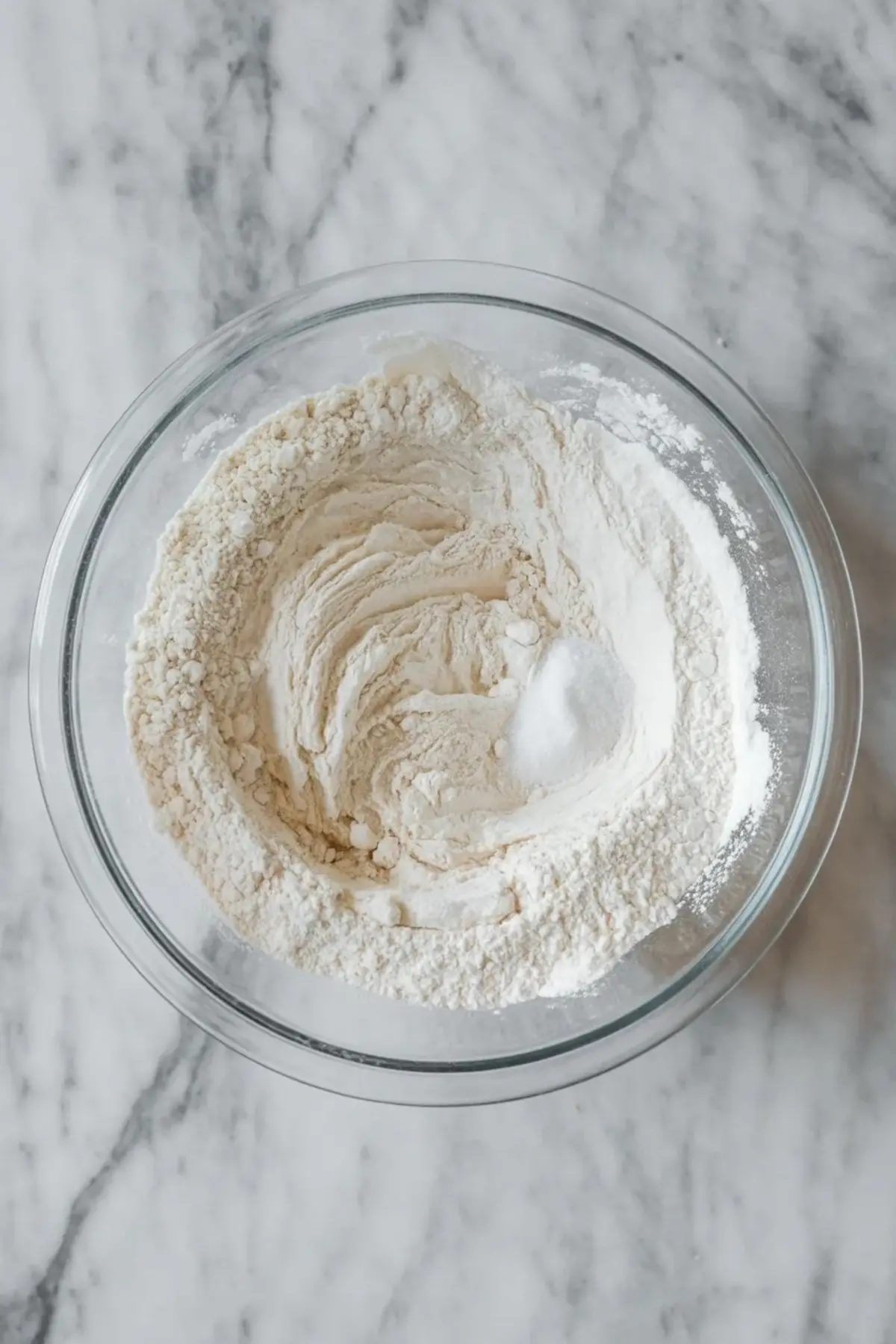 Flour, baking soda, and salt are whisked together in a glass bowl for maple pecan cookies before the dough is mixed.