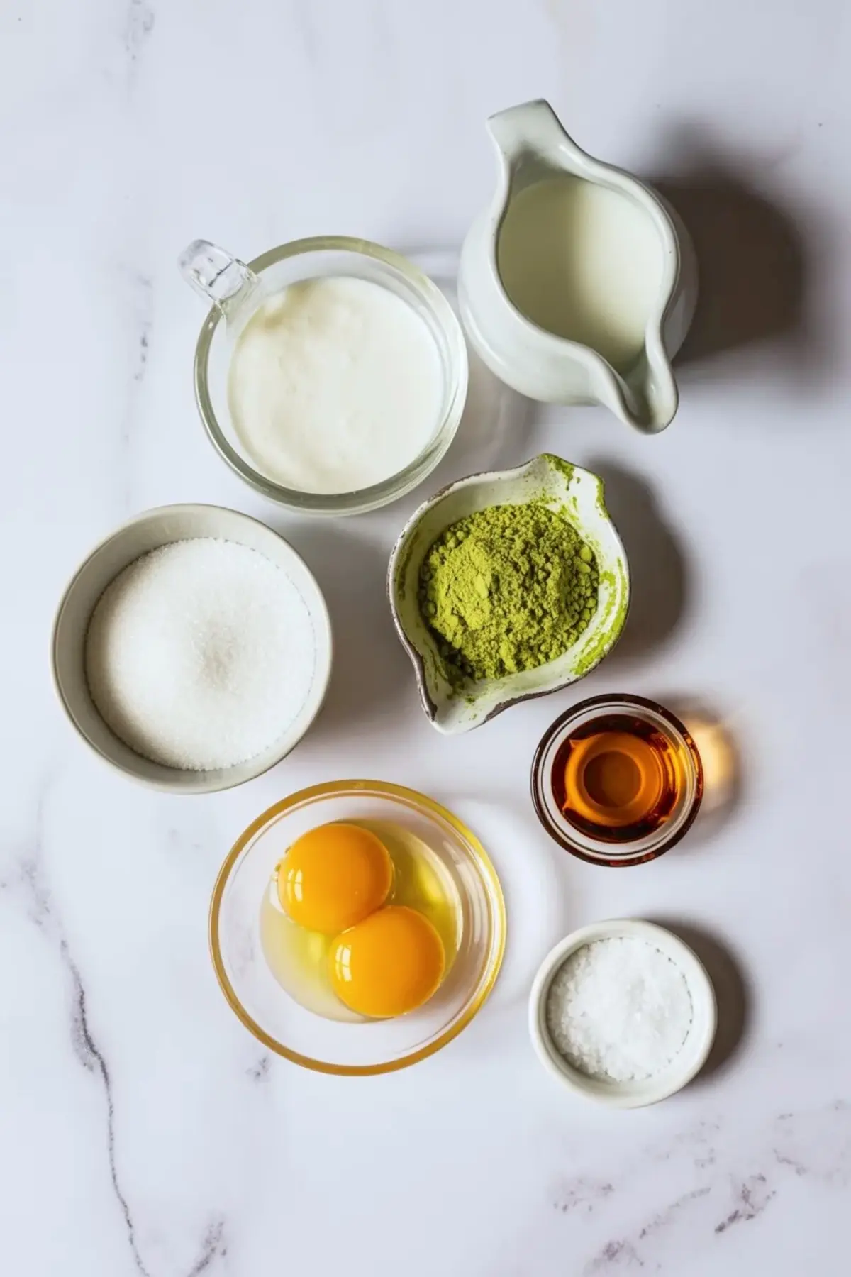 Ingredients for matcha ice cream arranged overhead with eggs, sugar, matcha powder, cream, milk, vanilla, and salt.