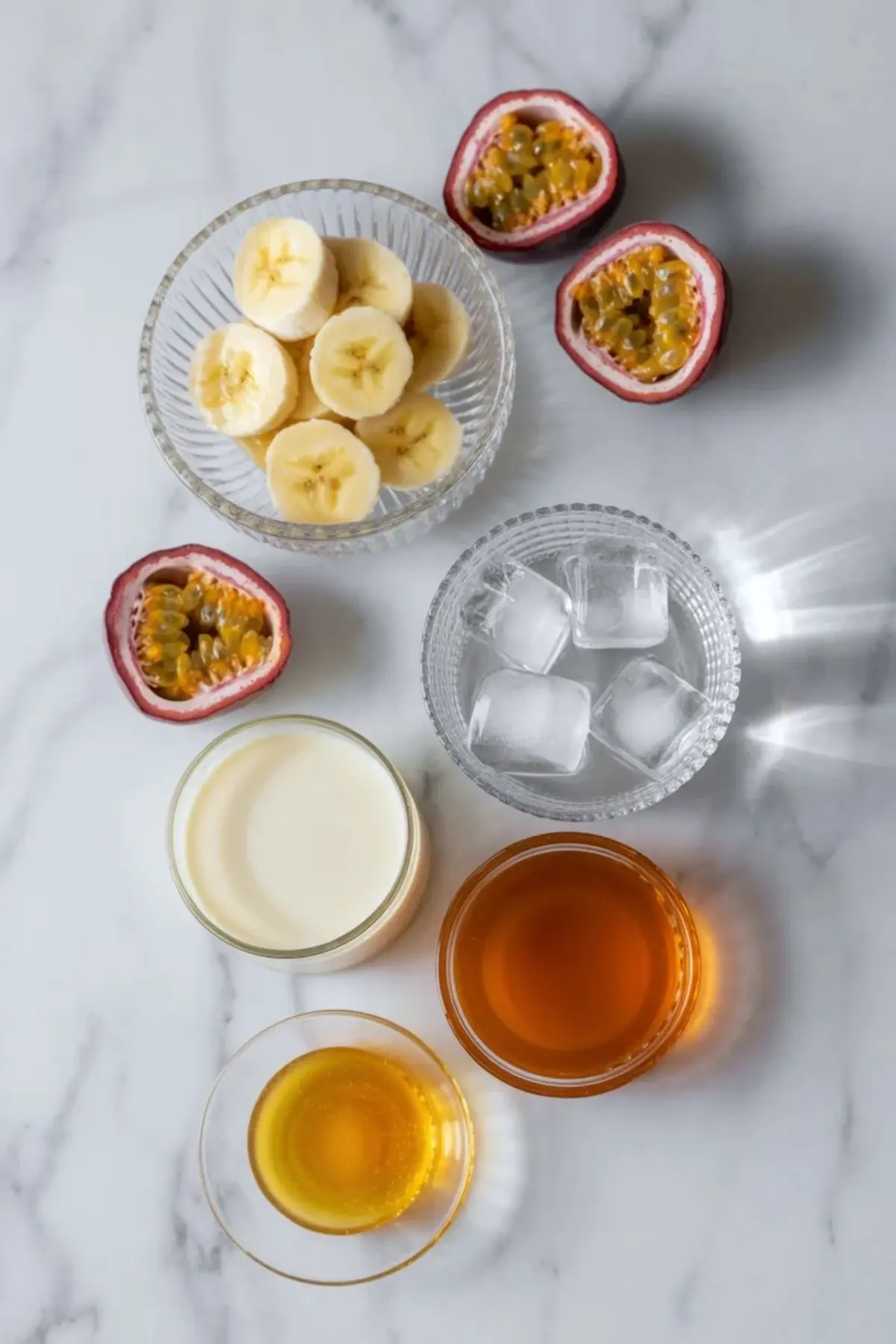 Ingredients for passion fruit juice recipe with banana on white marble with sliced banana, passion fruits, ice, sweetener, and creamy liquid for blending.