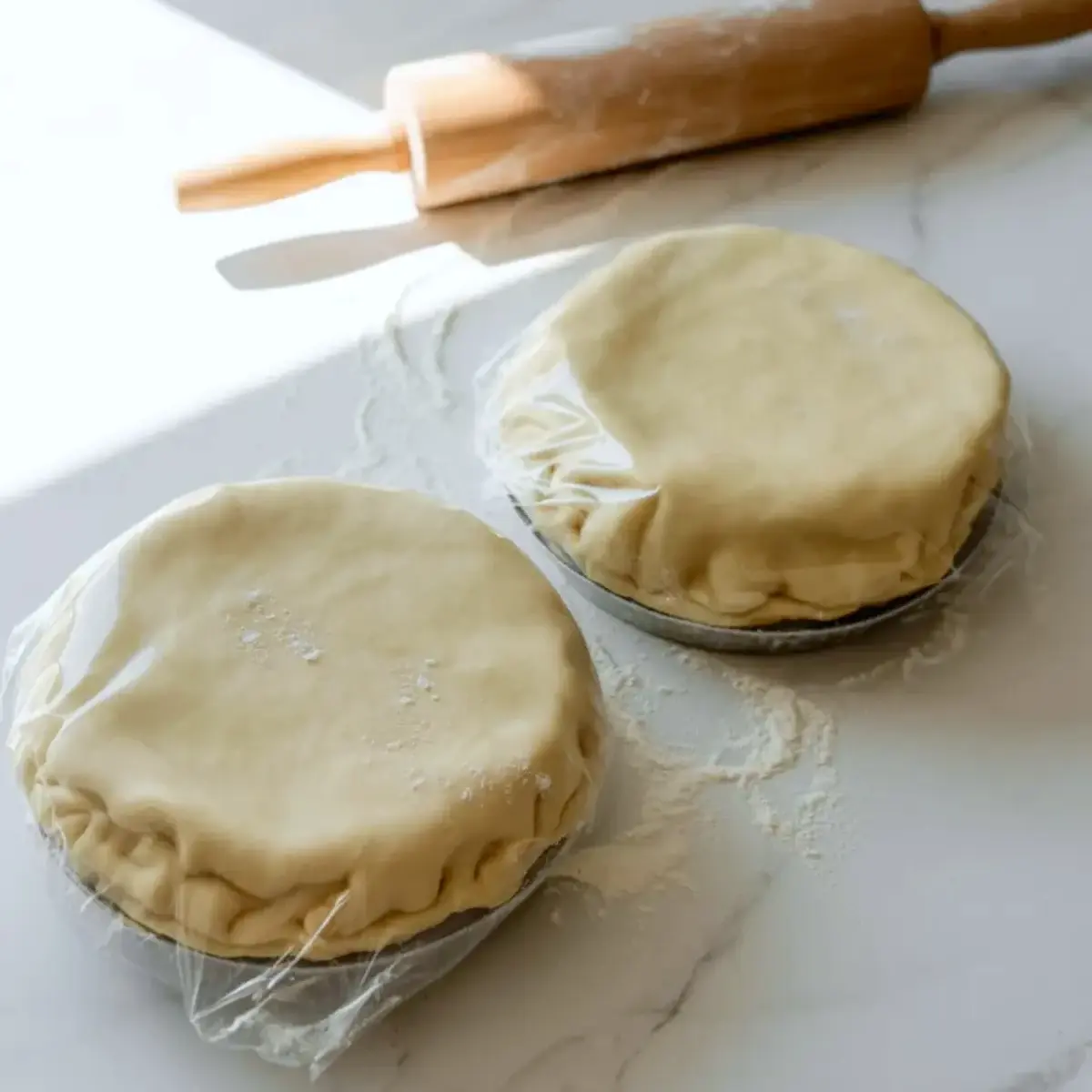 Prepared pie crust rounds for peach mango pie resting in pans under plastic wrap before filling and baking.