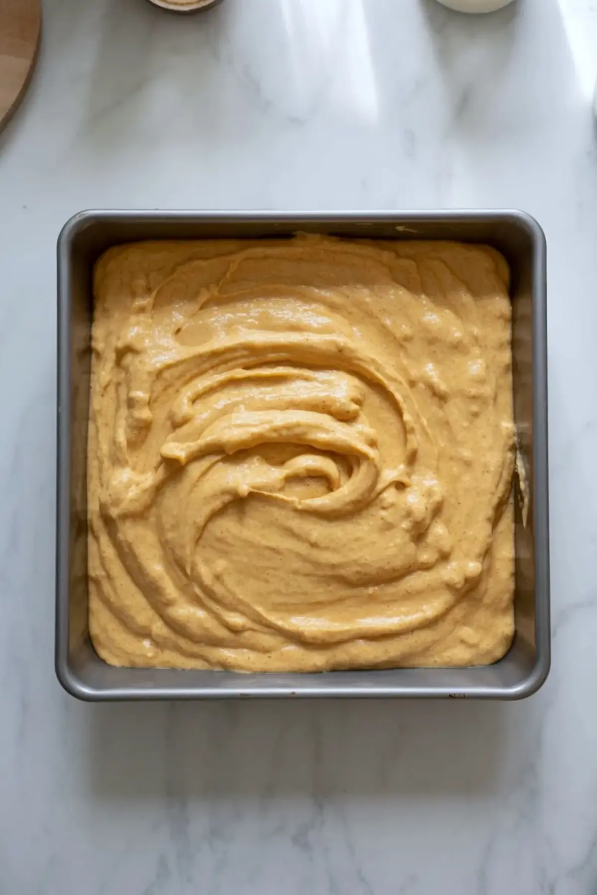 Pumpkin cornbread batter spread in a square baking pan before baking.