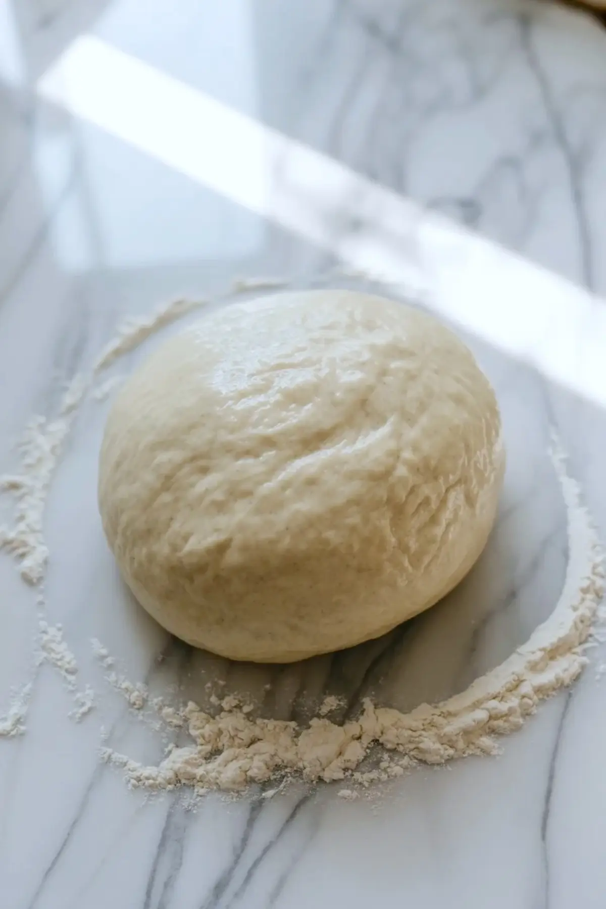 Smooth kneaded sourdough bagel dough ball resting on a floured marble surface before shaping.