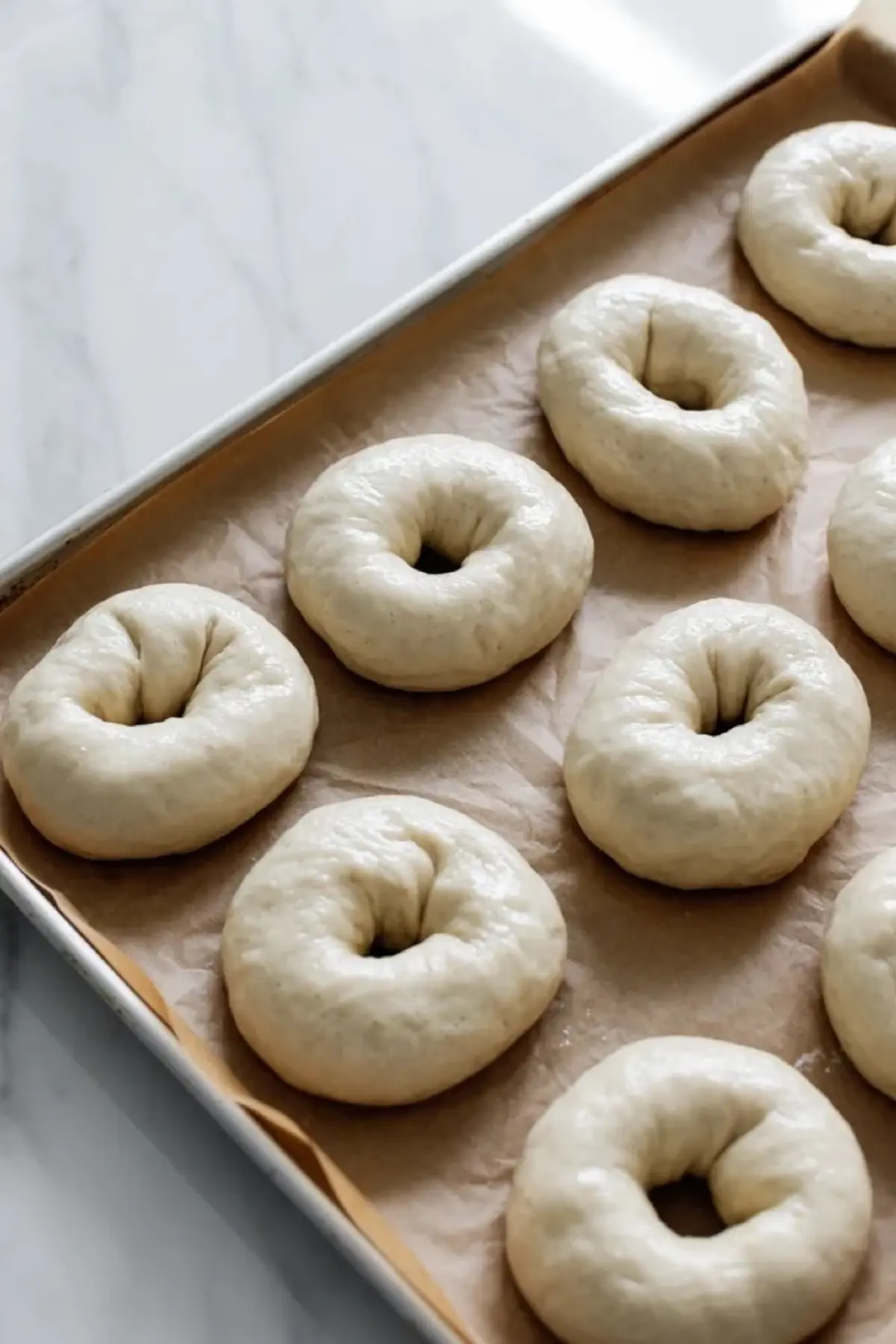 Shaped sourdough bagels on a parchment-lined baking sheet before boiling and baking.