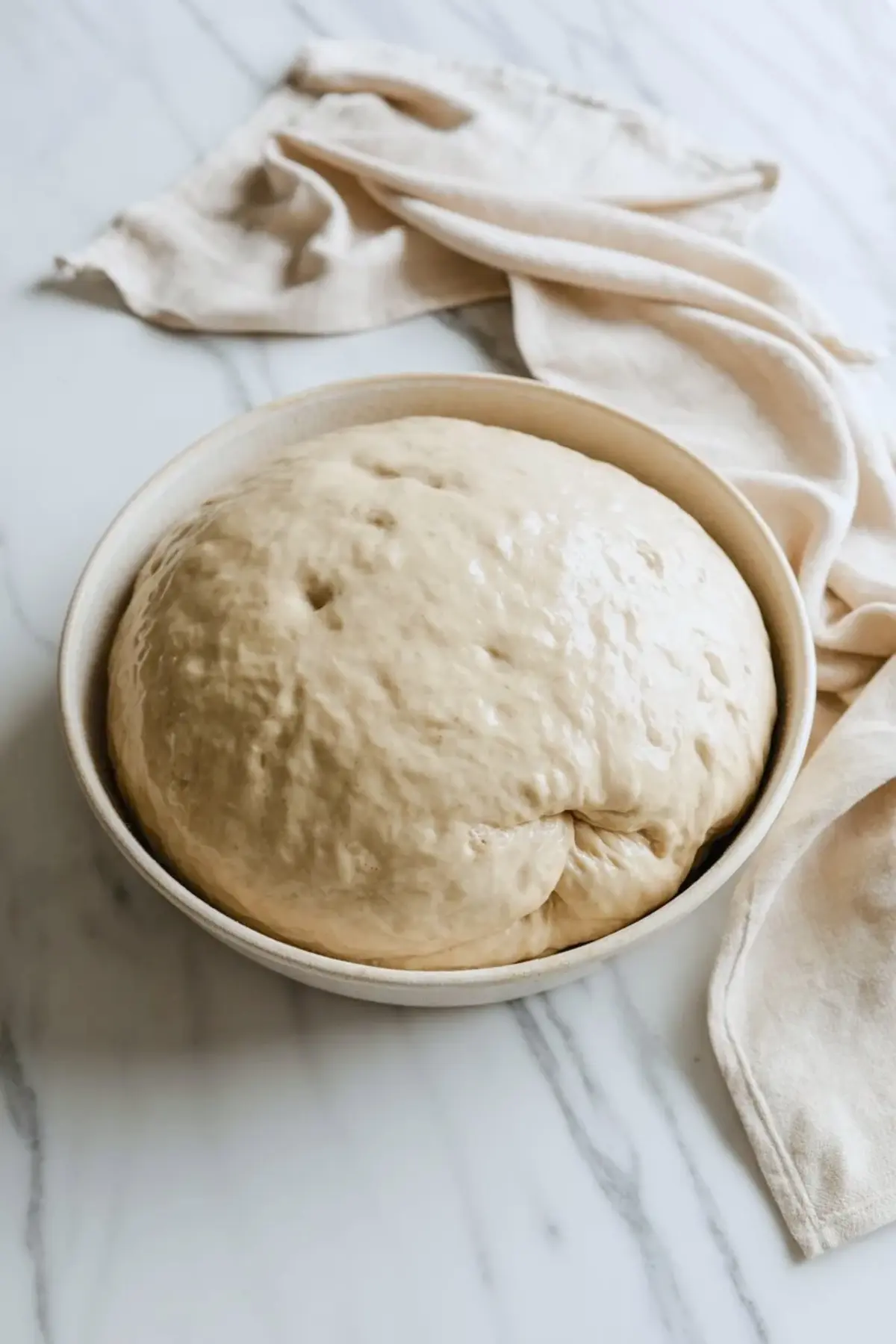 Sourdough donut dough after rising in a bowl, showing a soft puffy texture before chilling and shaping.