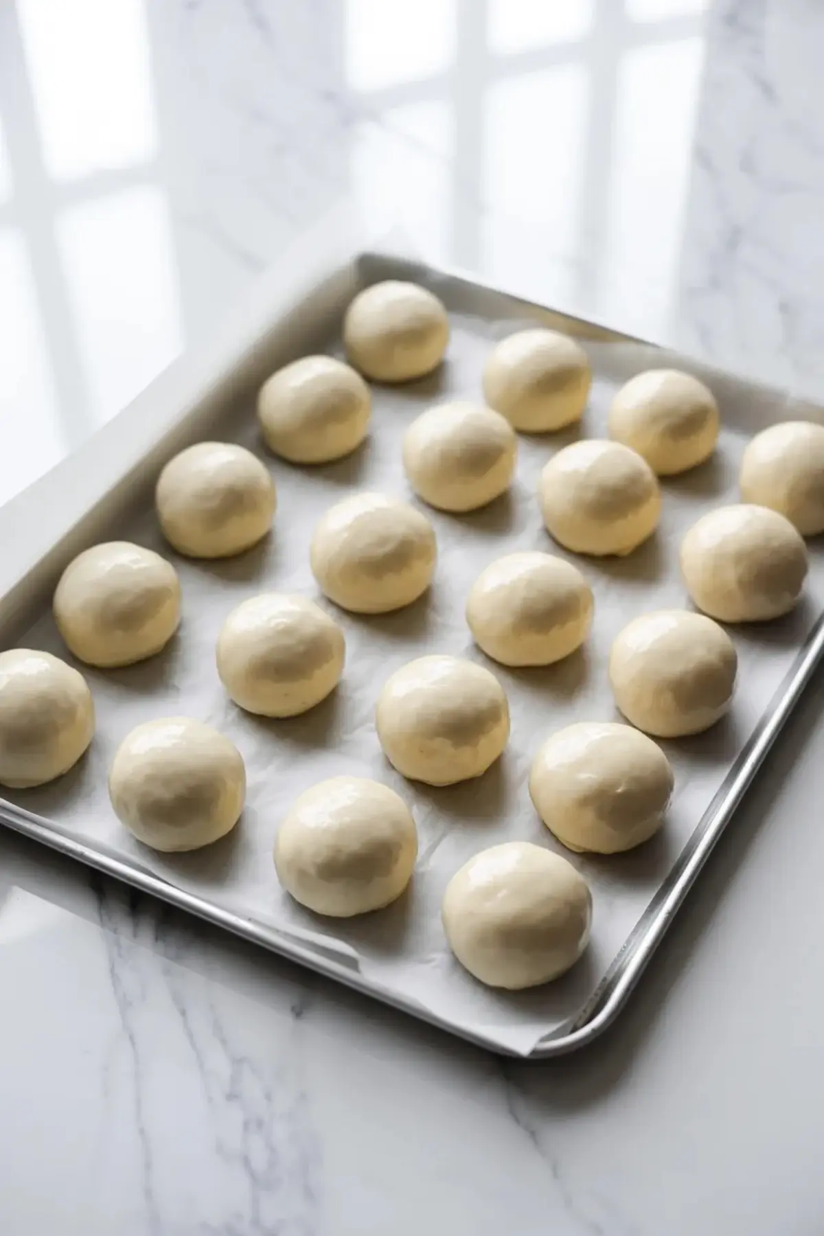Shaped sourdough donut holes on a tray, proofed into smooth round balls before frying.