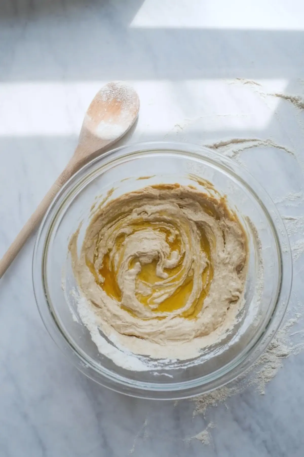 Sourdough English muffin dough mixing in a bowl with a spoon during the early dough stage.