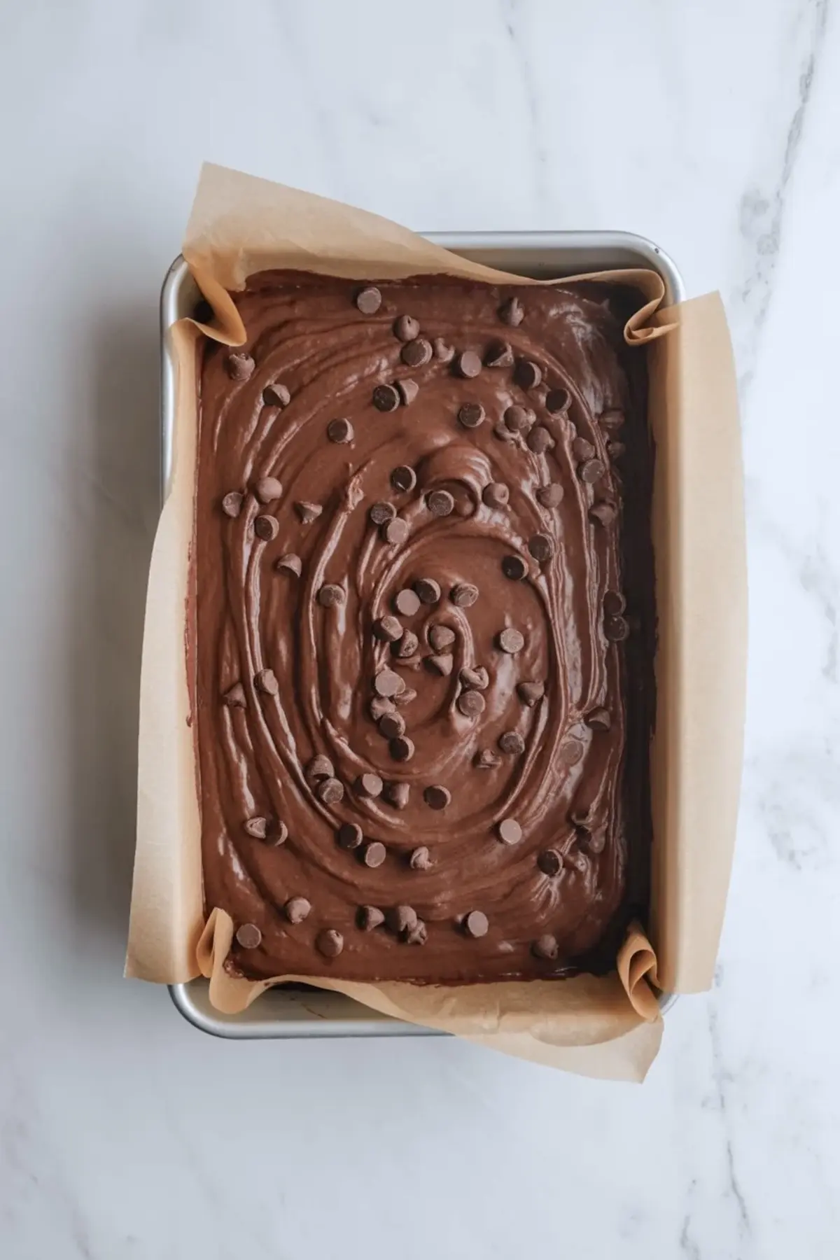 Star-spangled brownie batter is spread in a parchment-lined pan with chocolate chips before baking.