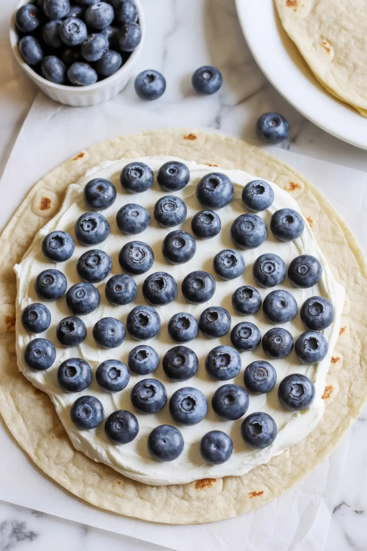 Blueberries scattered over cream cheese filling on a tortilla before cooking blueberry breakfast quesadillas.