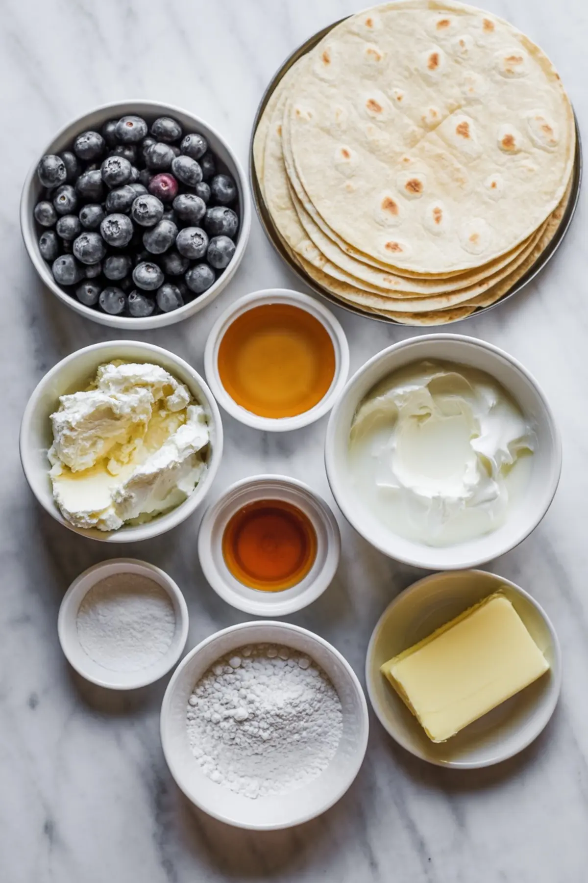 Ingredients for blueberry breakfast quesadillas arranged with tortillas, blueberries, cream cheese, Greek yogurt, honey, butter, and powdered sugar.